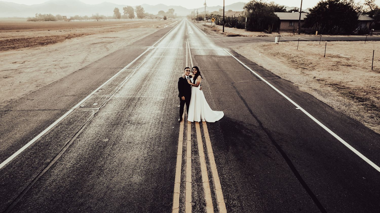 Romantic wedding photo of couple standing on empty rural road at sunset.