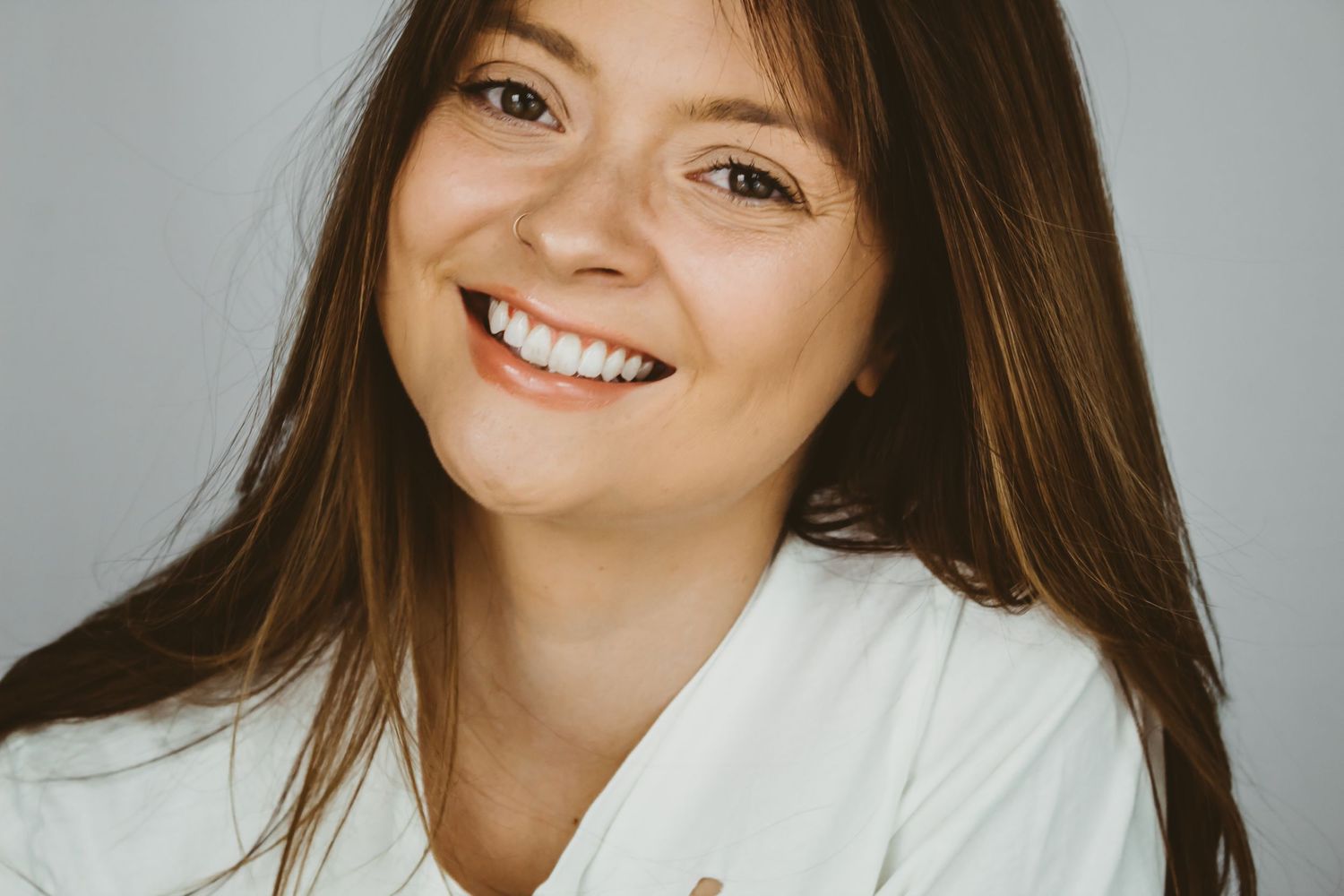 A warm portrait of someone in a white top with long brown hair against a neutral background.