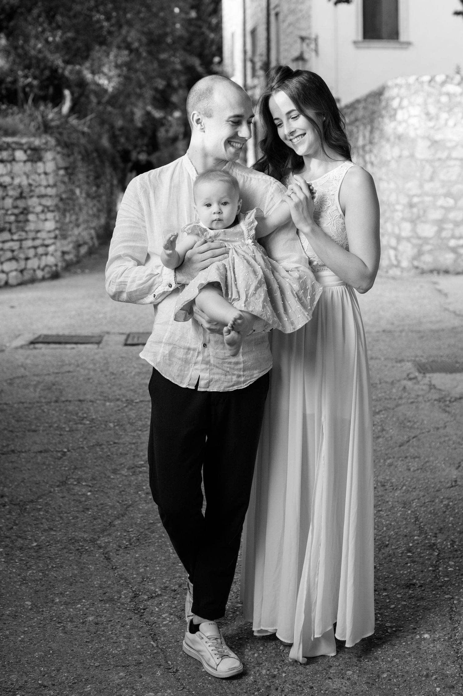 A tender black and white family portrait captured outdoors against a rustic brick wall setting.