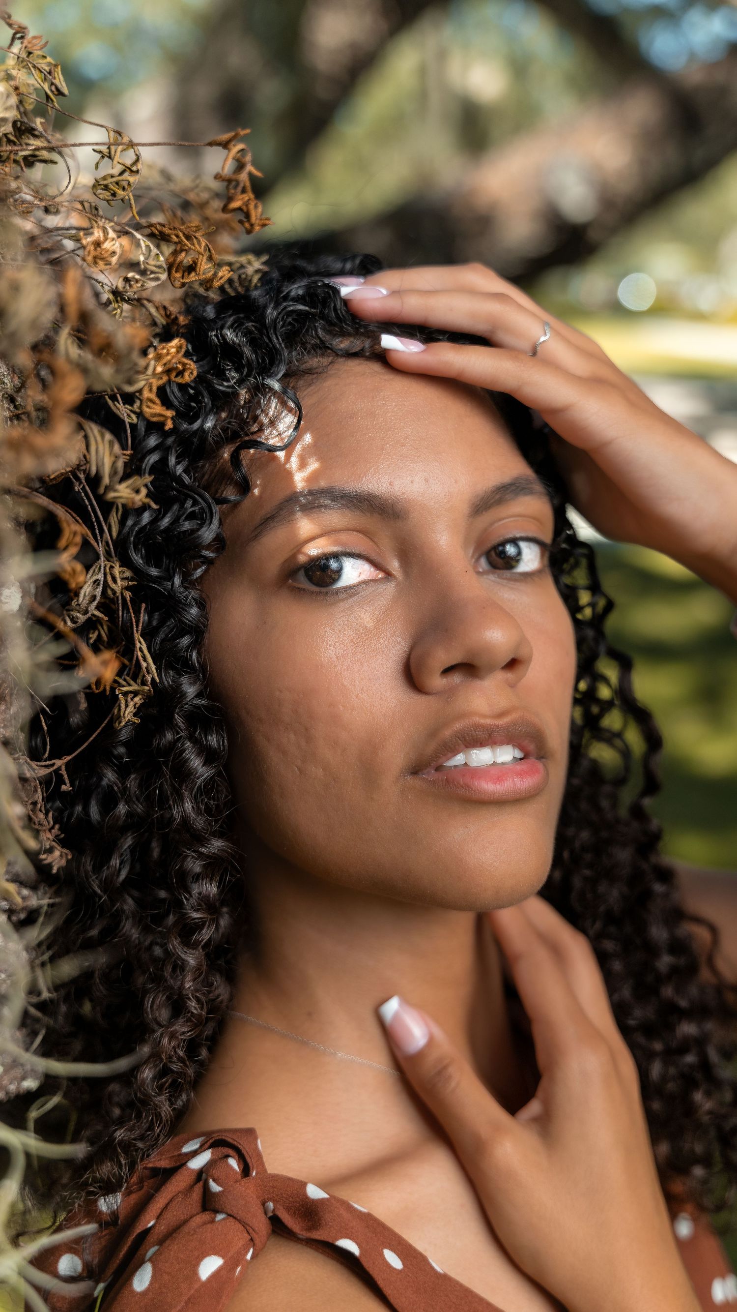 Portrait of woman with natural curly hair in brown polka dot dress outdoors.