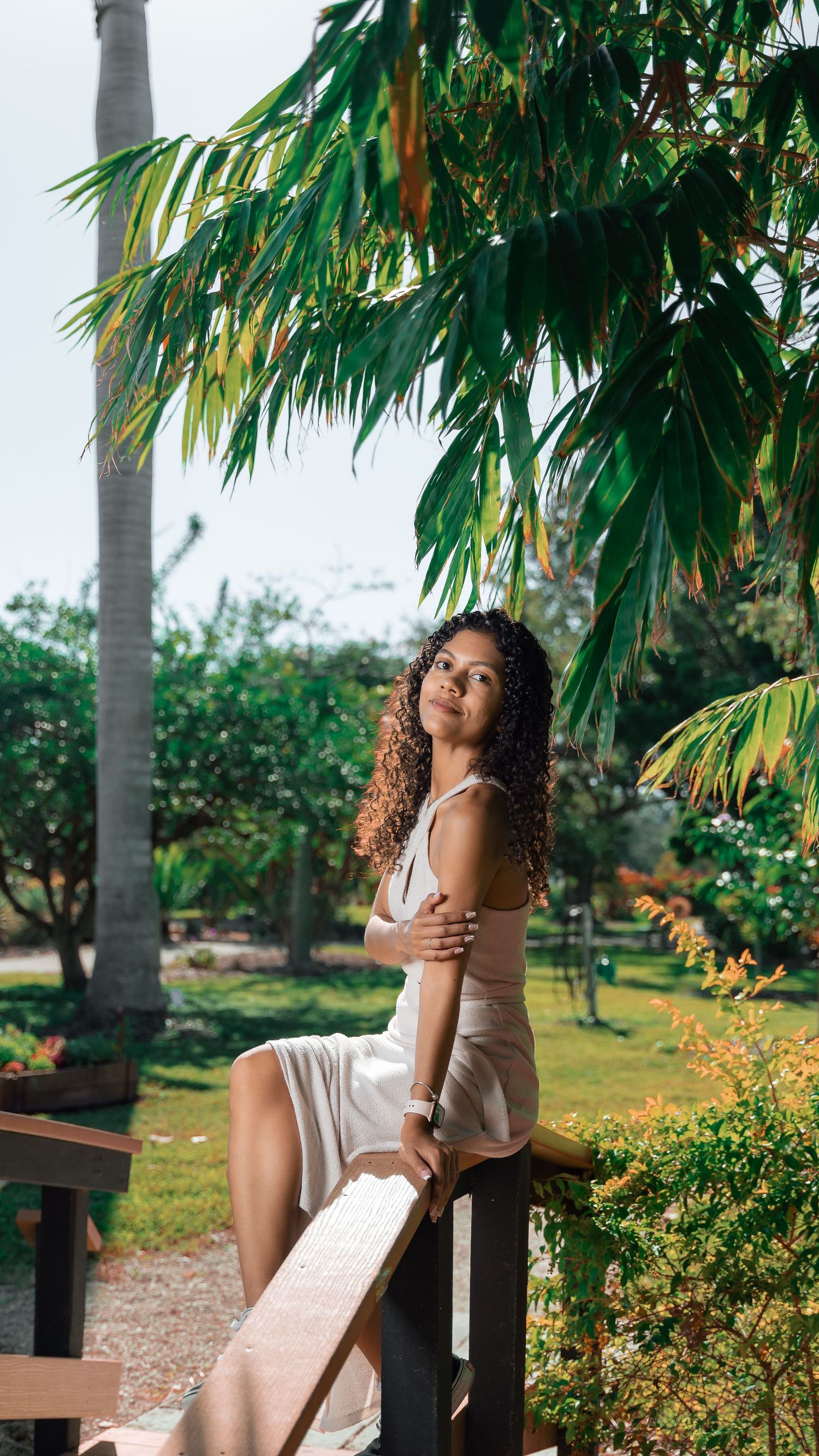 Elegant pose in a white dress by a wooden railing surrounded by tropical palm trees.