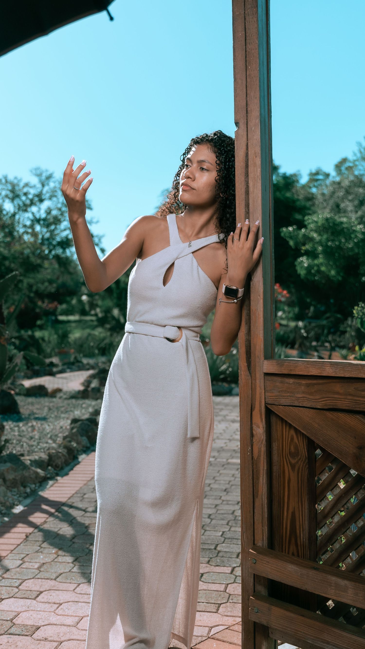 A white halter maxi dress worn elegantly on a patio with wooden posts against a blue sky.