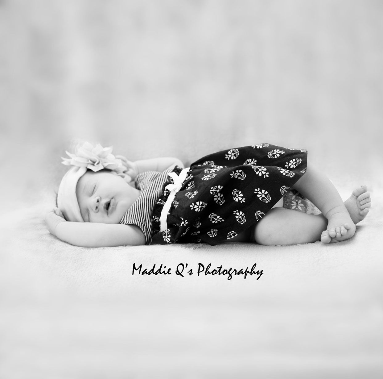 A sleeping infant wearing a black and white patterned dress and headband on a light background.