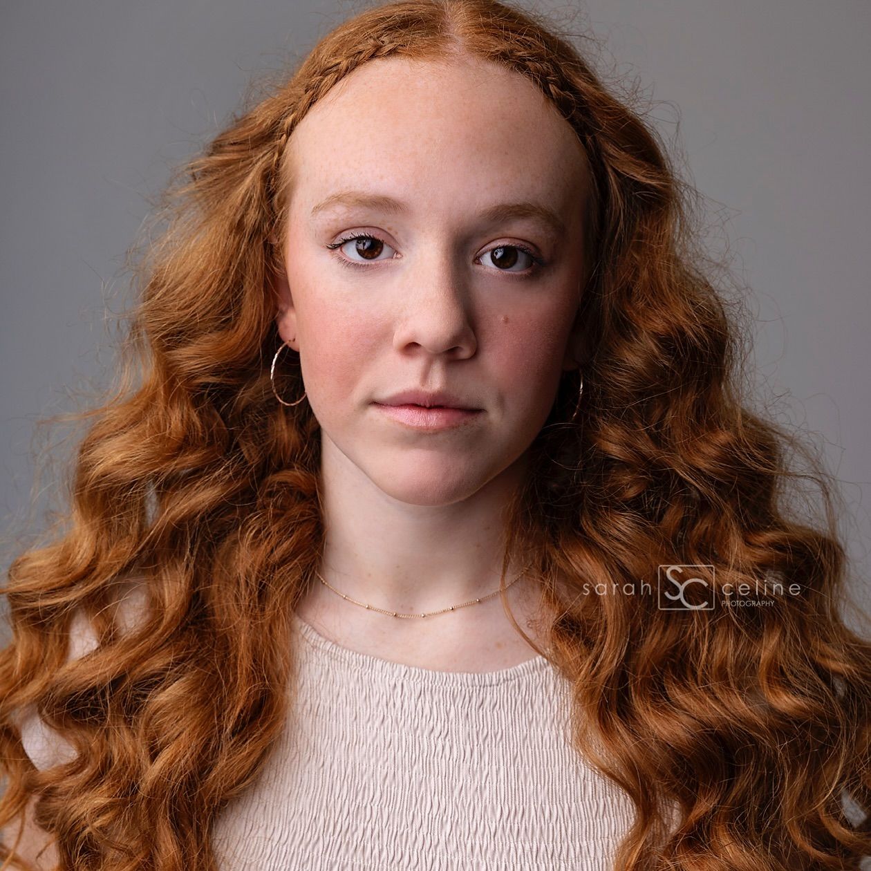 Portrait of young woman with long wavy red hair wearing a light pink top against gray background.