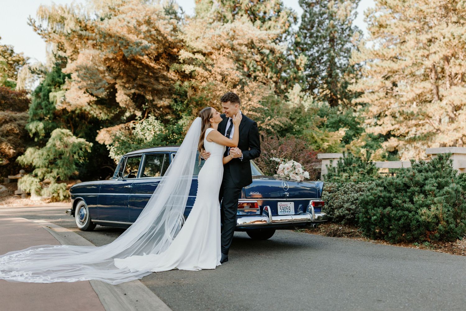 Bride and groom smiling next to a vintage Mercedes car at Point Defiance Rose Garden in Tacoma