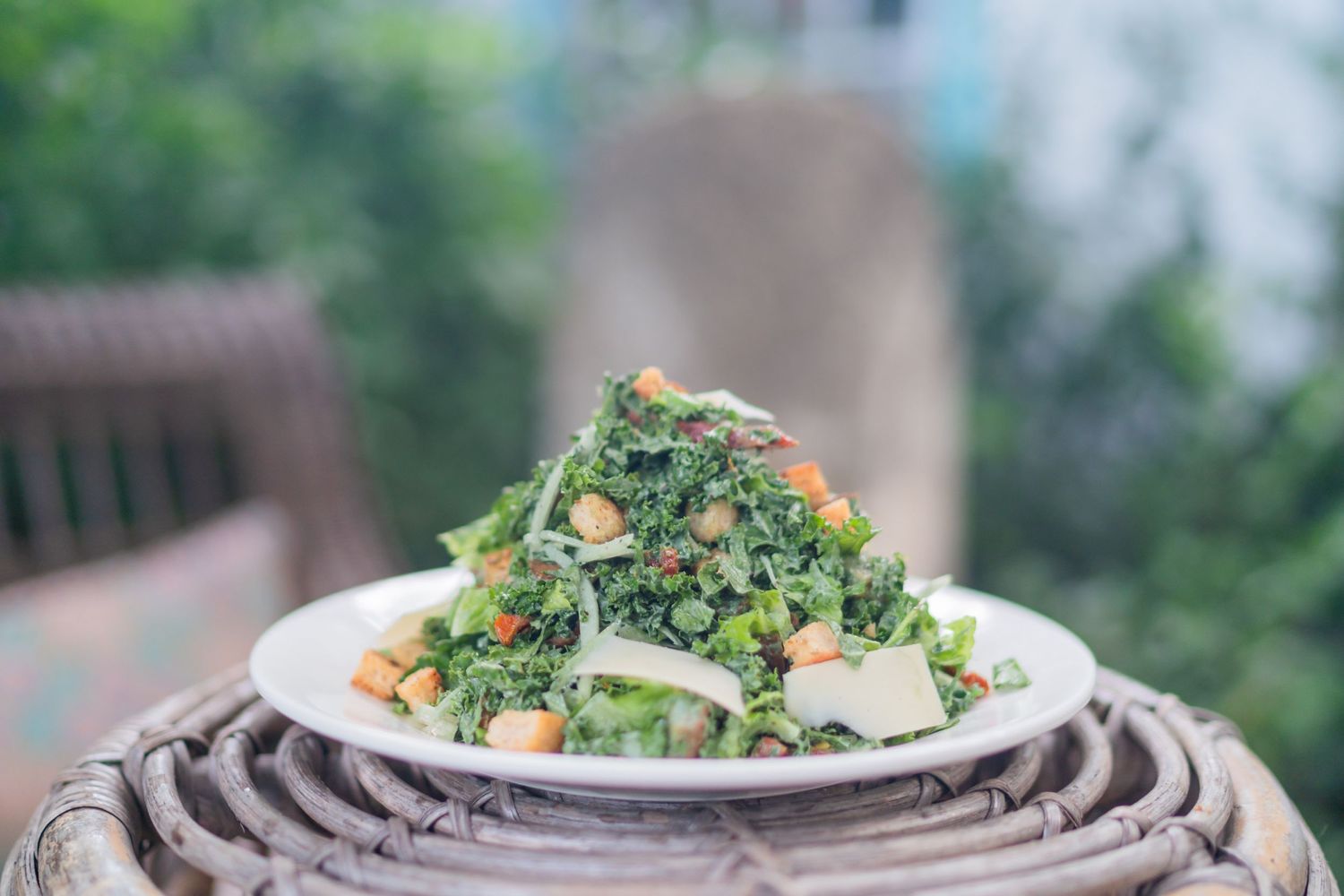 A fresh kale salad topped with nuts served on a white plate atop a wooden surface outdoors.