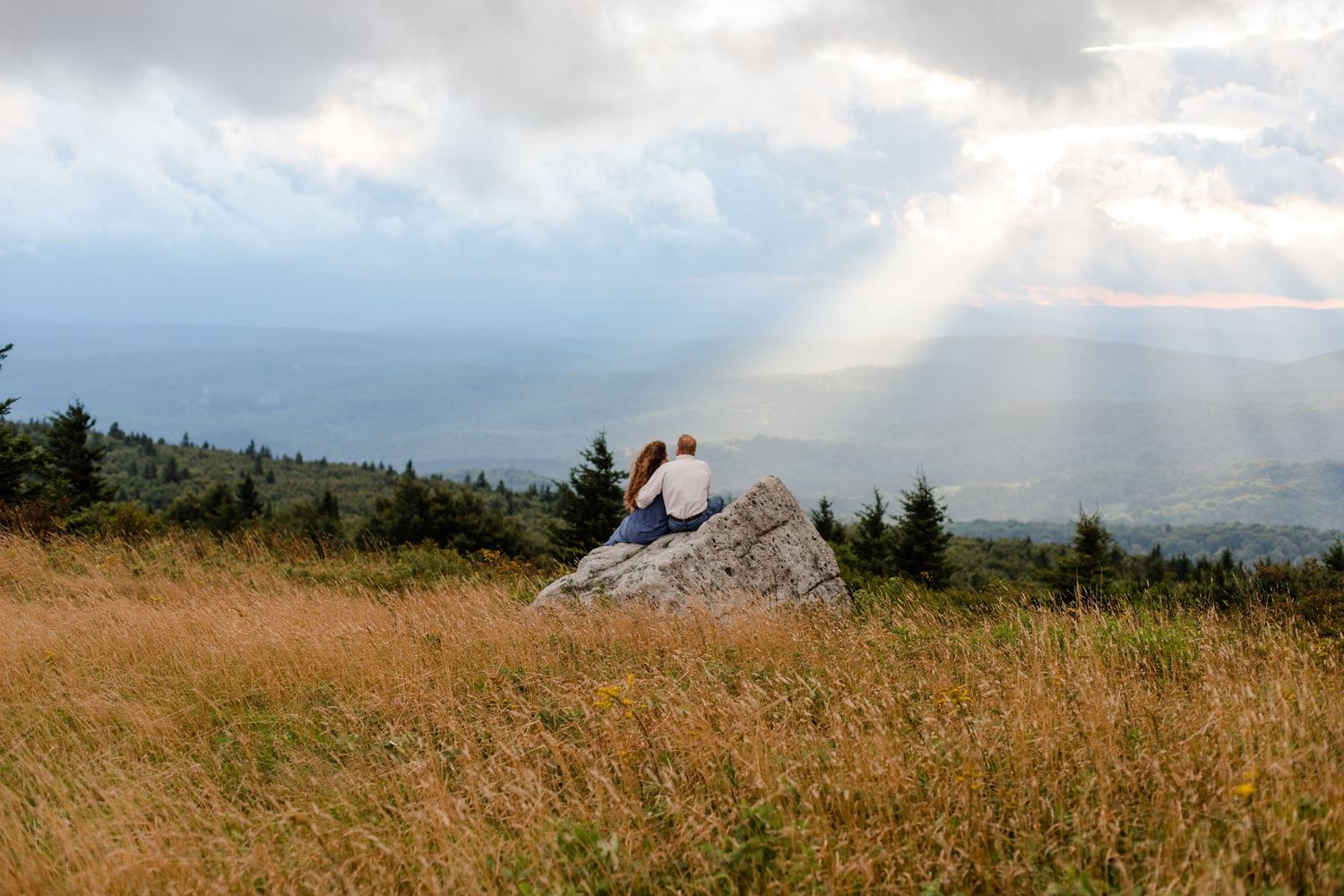 Dramatic mountain vista with sunbeams breaking through clouds over rolling hills.