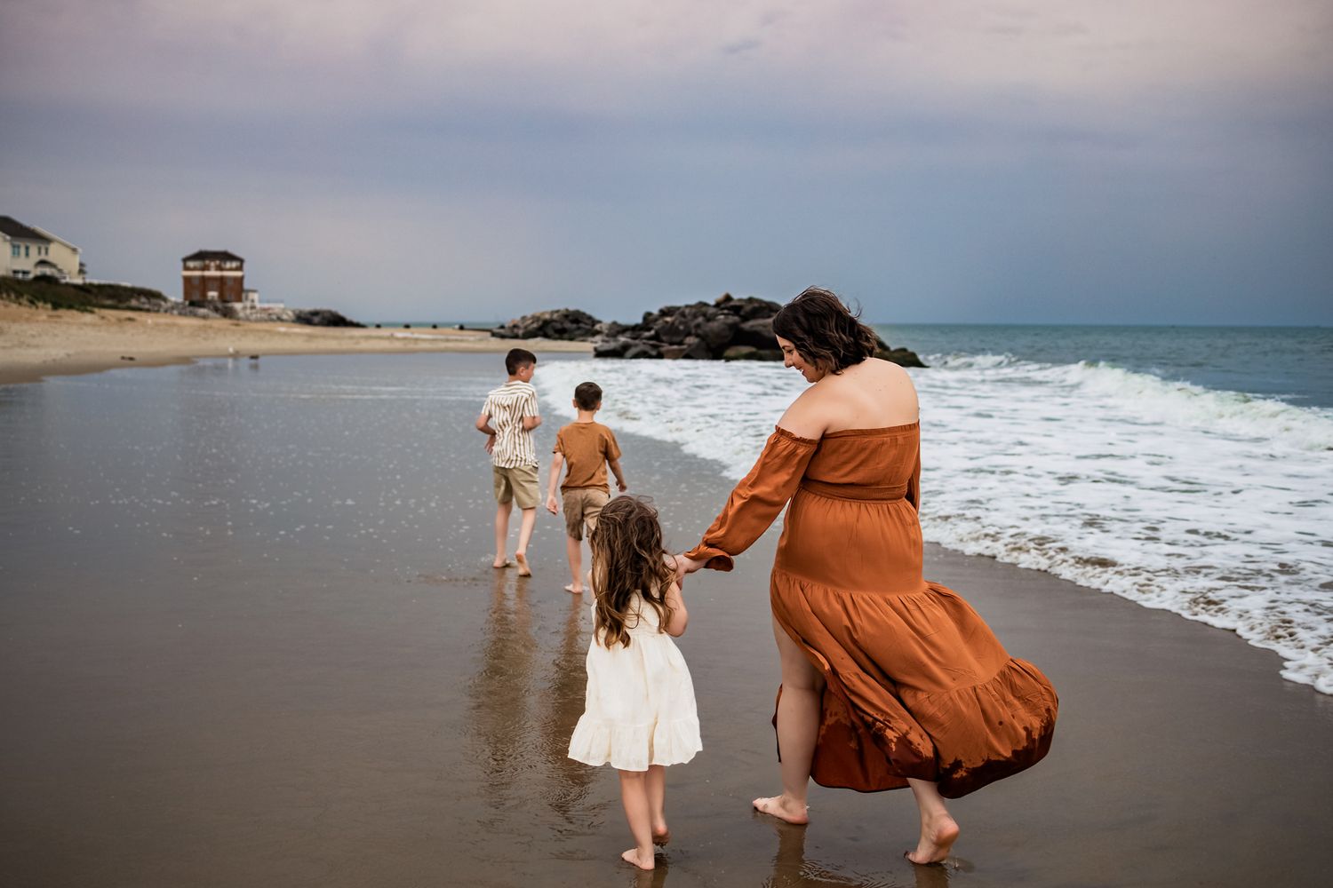 People walking along a scenic beach shoreline at sunset with waves crashing nearby.
