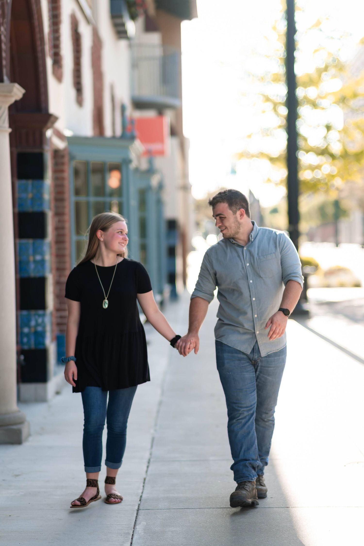 Couple holding hands while walking down city sidewalk together.