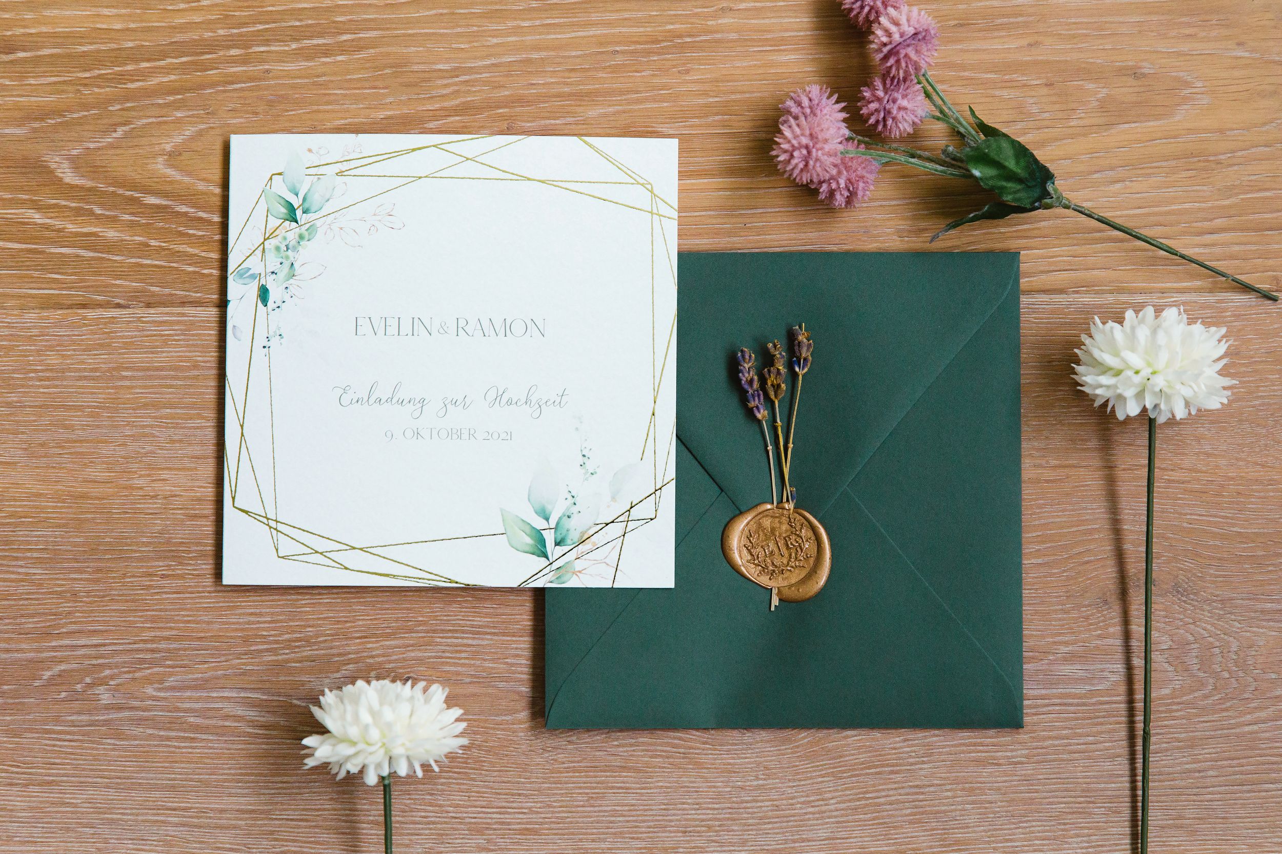 Minimalist wedding invitation suite with a dark green envelope and a gold wax seal.