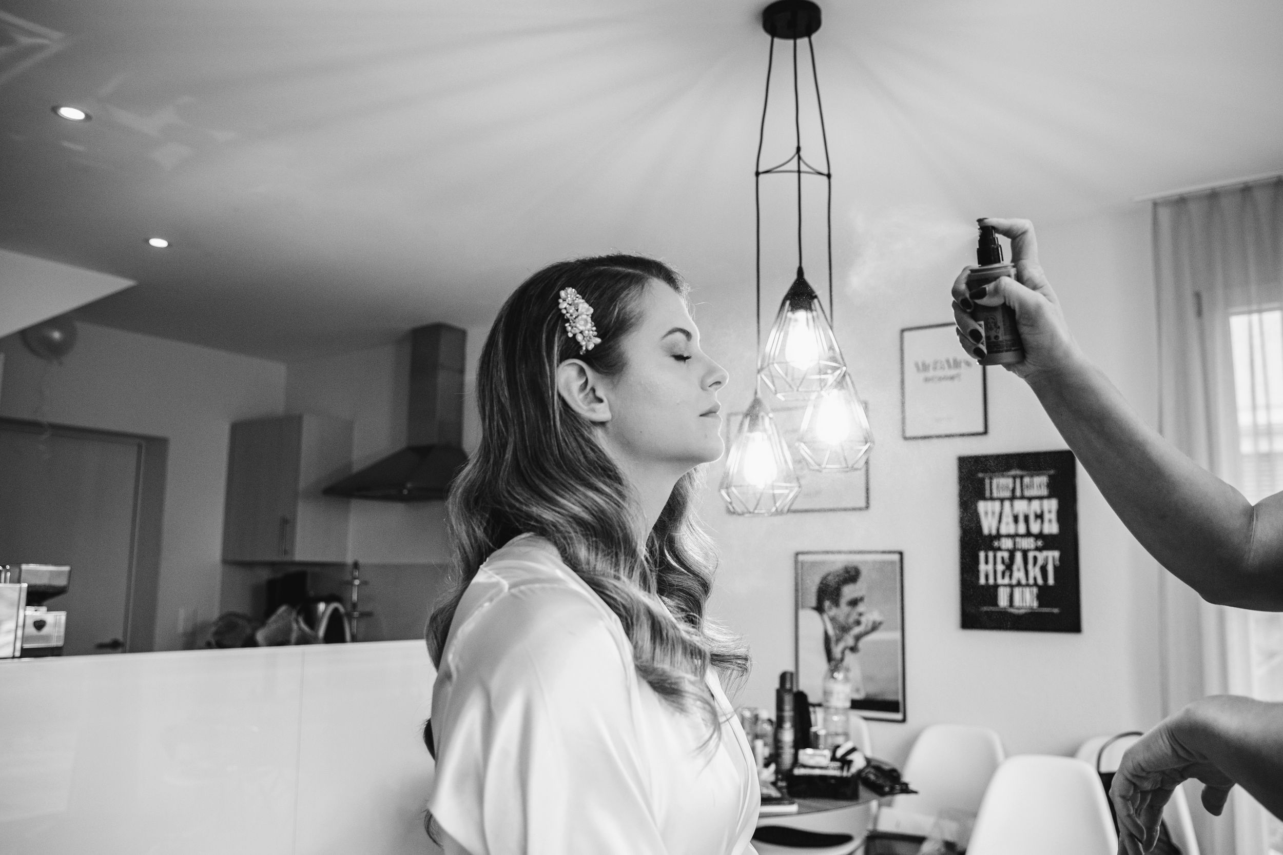 Black and white candid of a bride getting her hair styled while holding a glass of champagne.