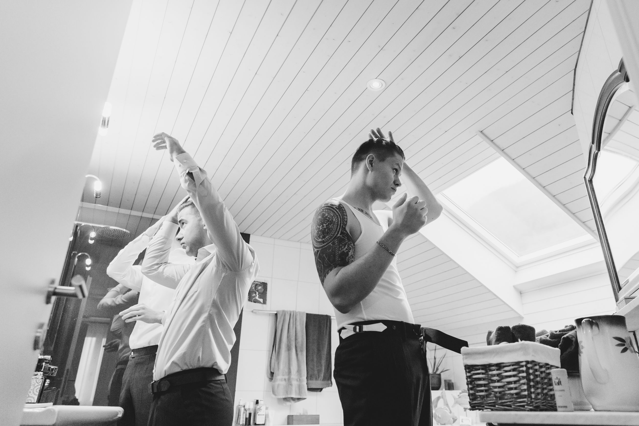 Wide black and white shot of a groom and his friends laughing and suiting up for a wedding morning.
