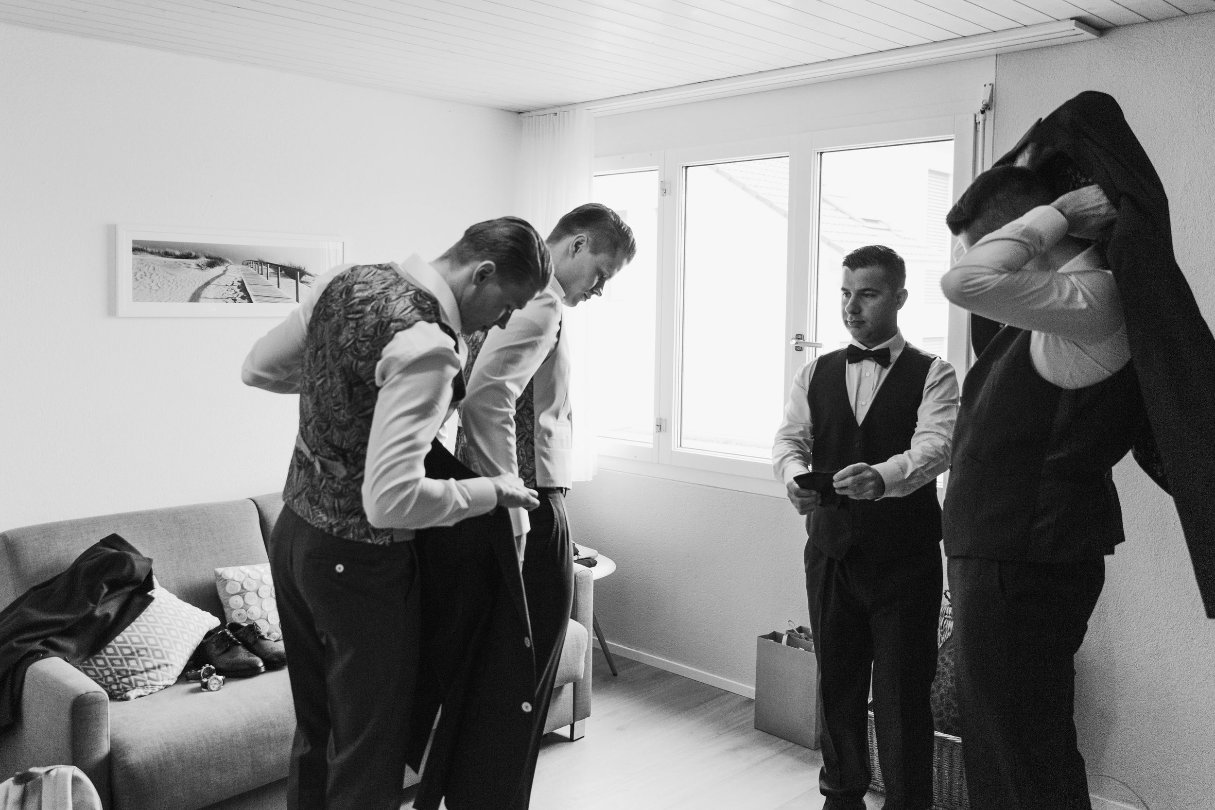Wide black and white shot of a groom and his wedding party getting ready in a bright, modern room.