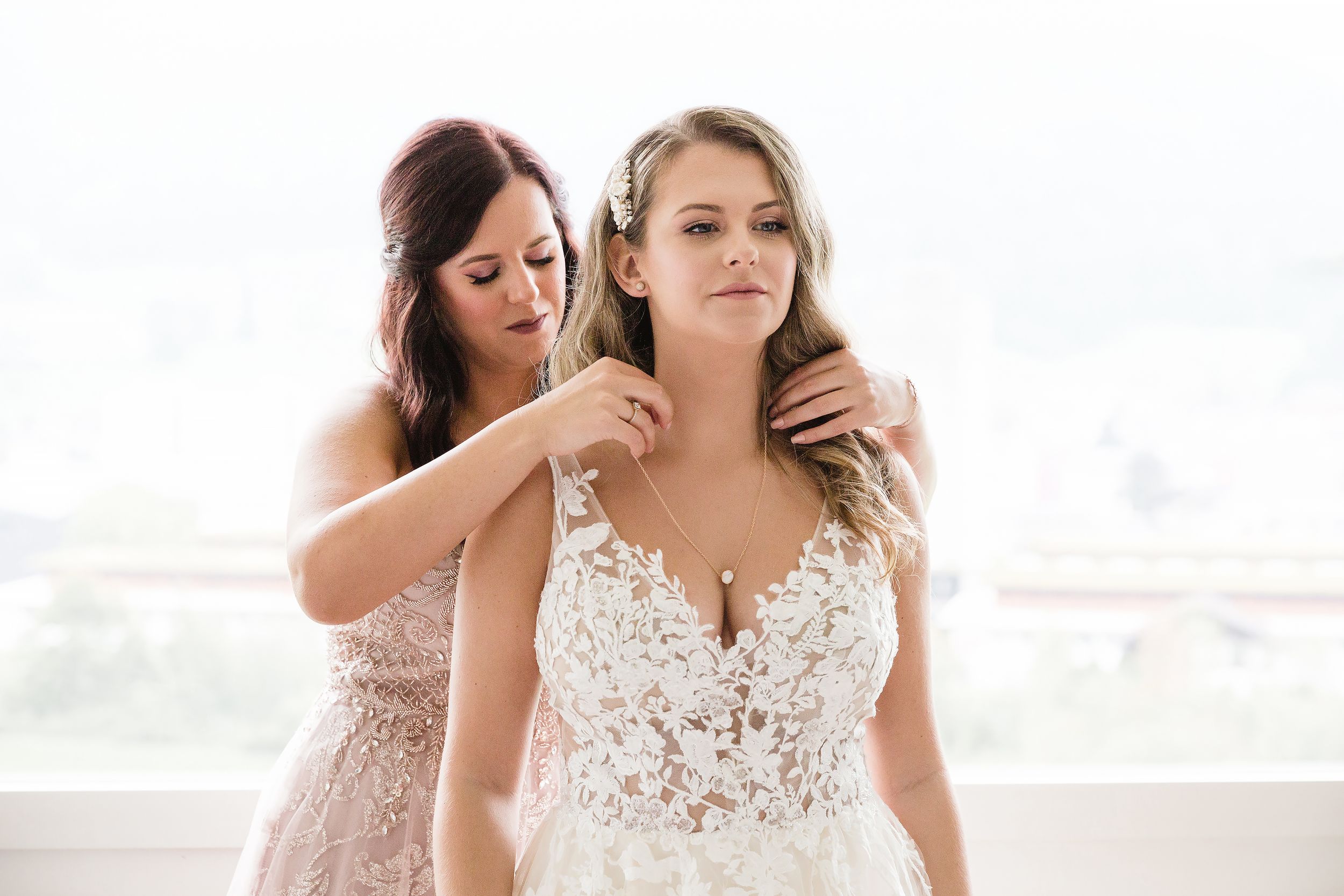 Candid shot of a bridesmaid assisting a bride with her jewelry during wedding preparations.