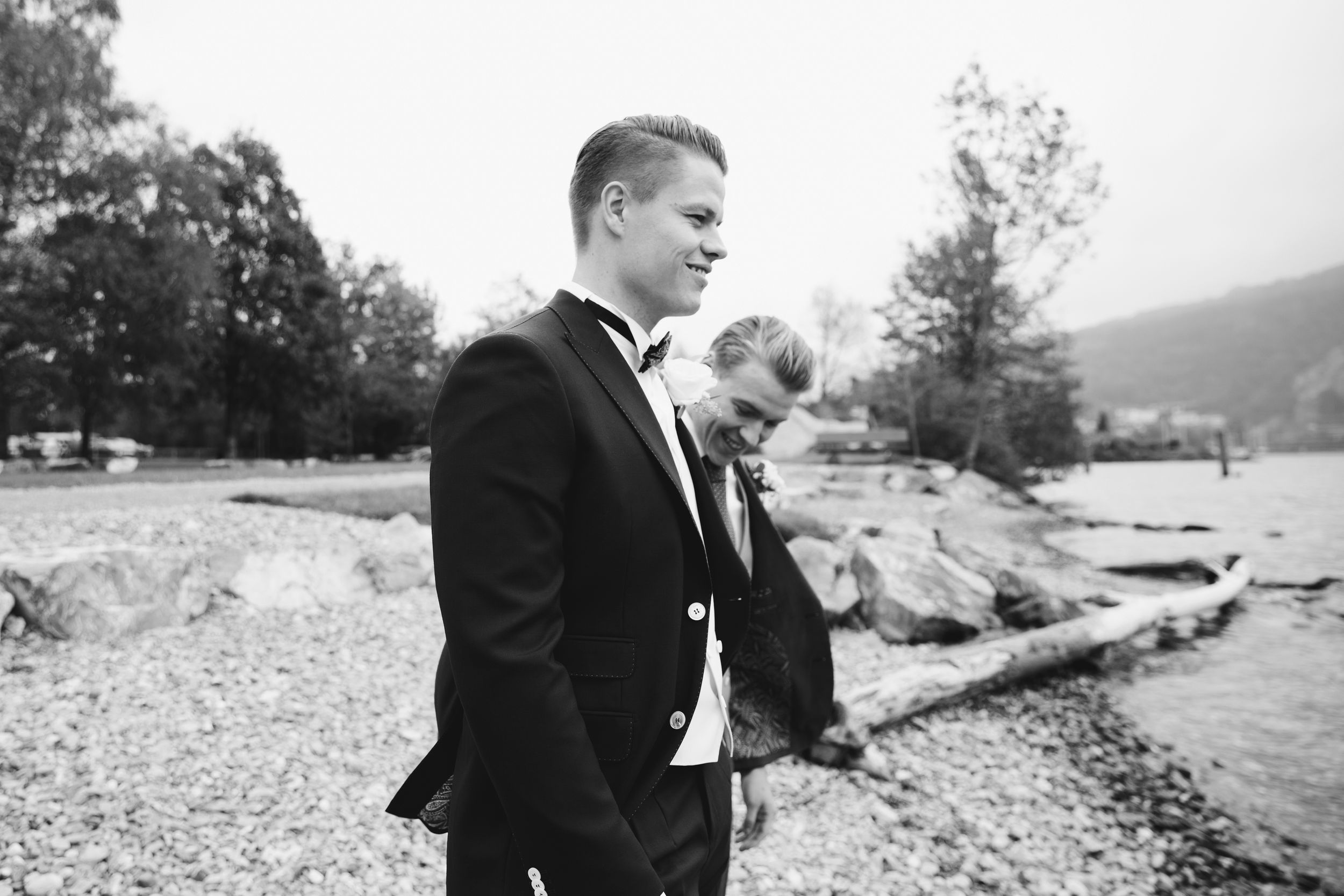 Black and white candid shot of a groom and a young guest walking together along a lakeside path.