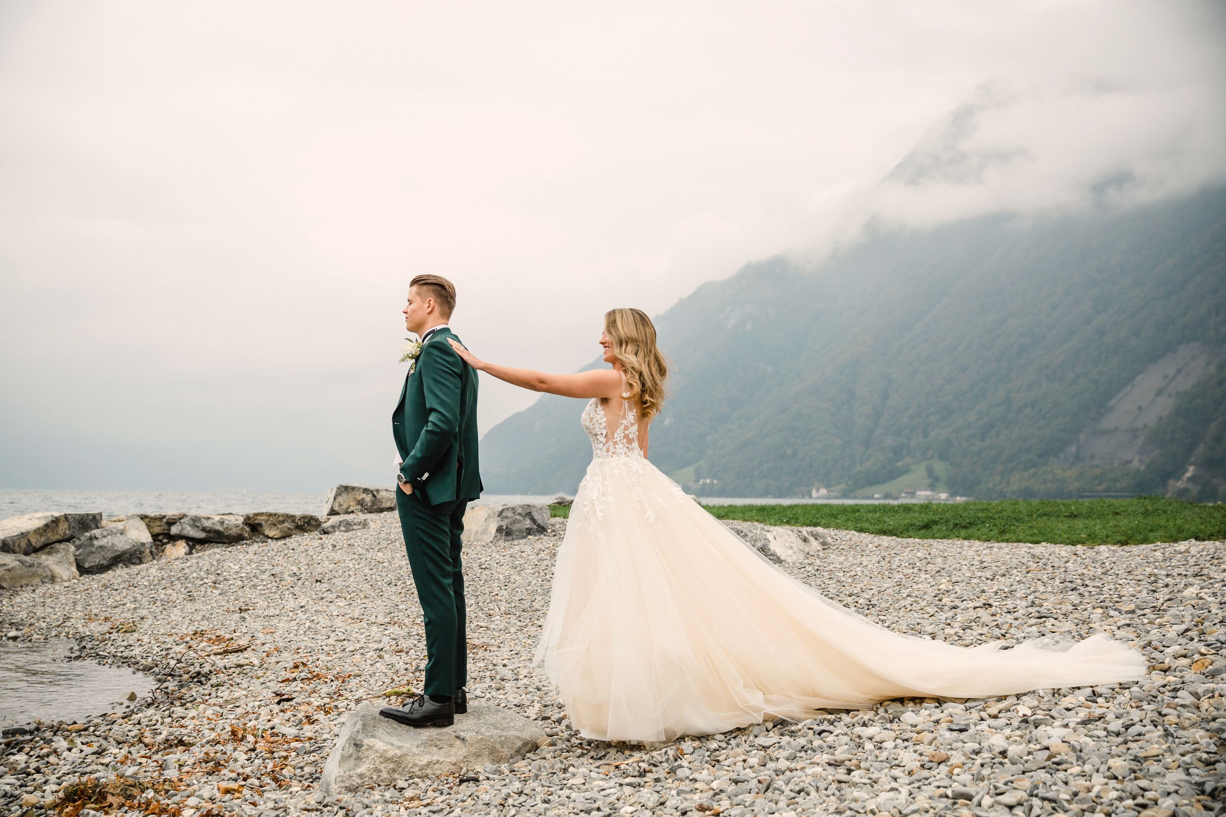 Full-length shot of a bride and groom holding hands while walking along a scenic, rocky shoreline.