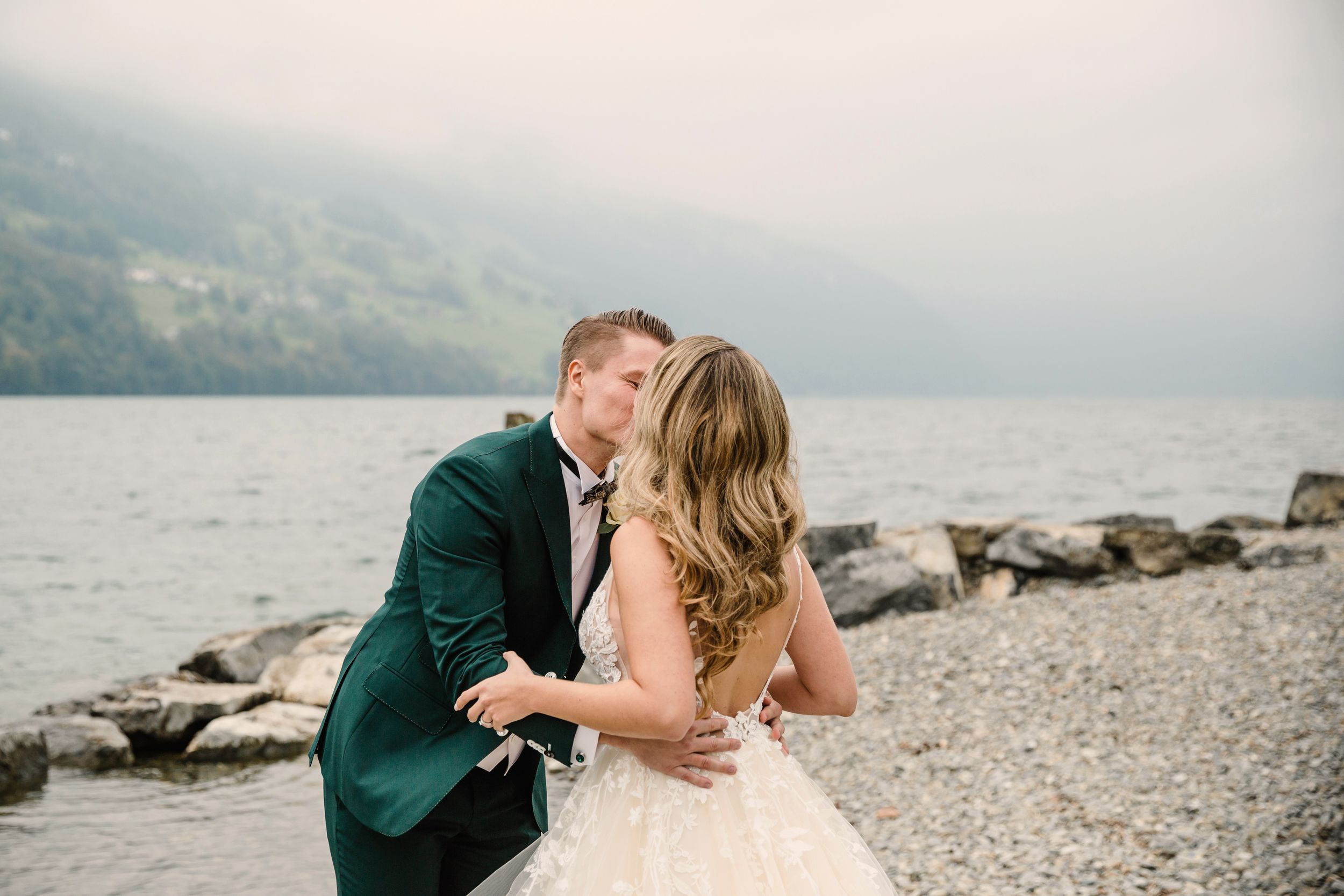 Candid portrait of a bride and groom kissing during their outdoor wedding session by the lake.