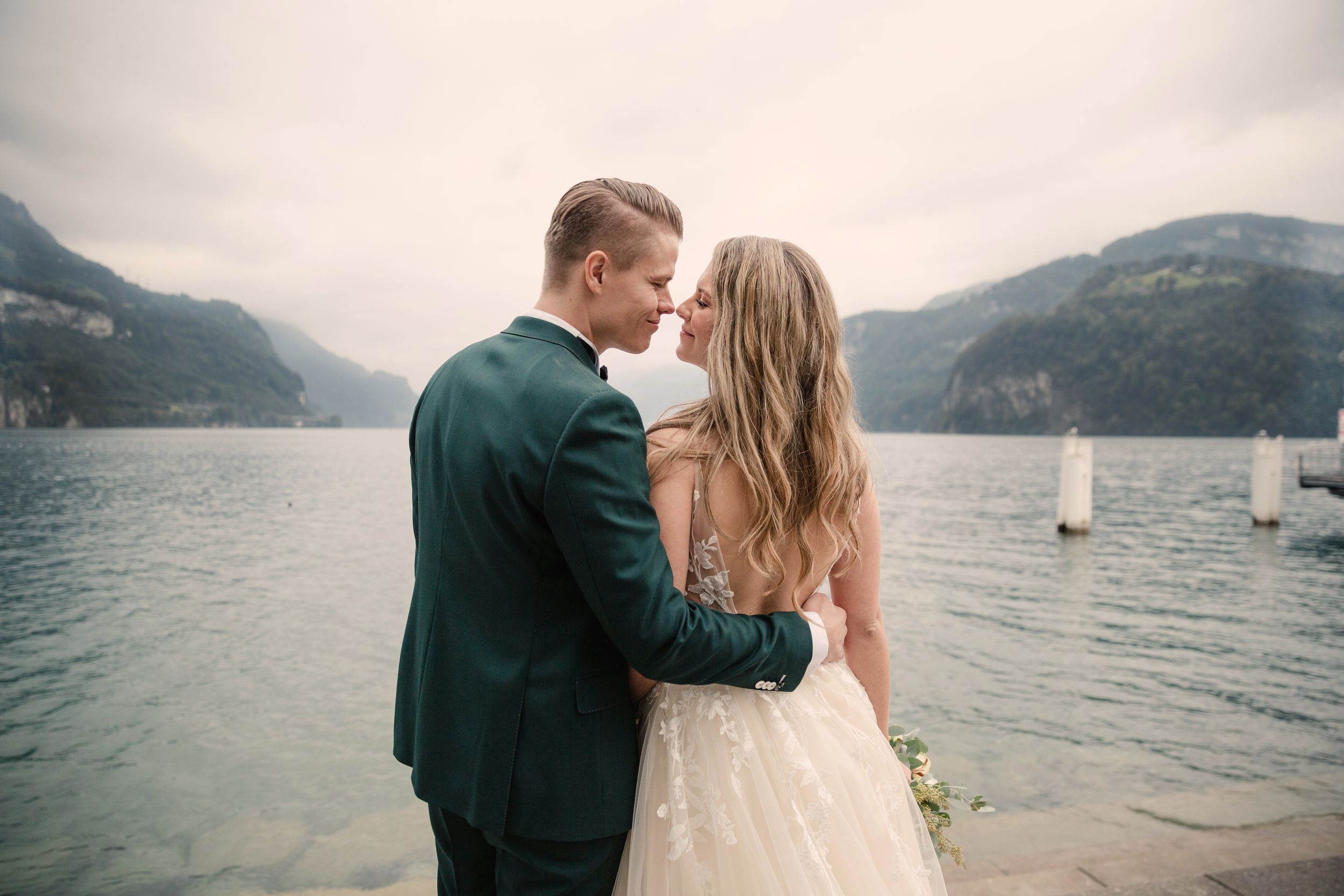 Close-up of a groom kissing his bride's forehead on a lakeside dock during a scenic wedding shoot.
