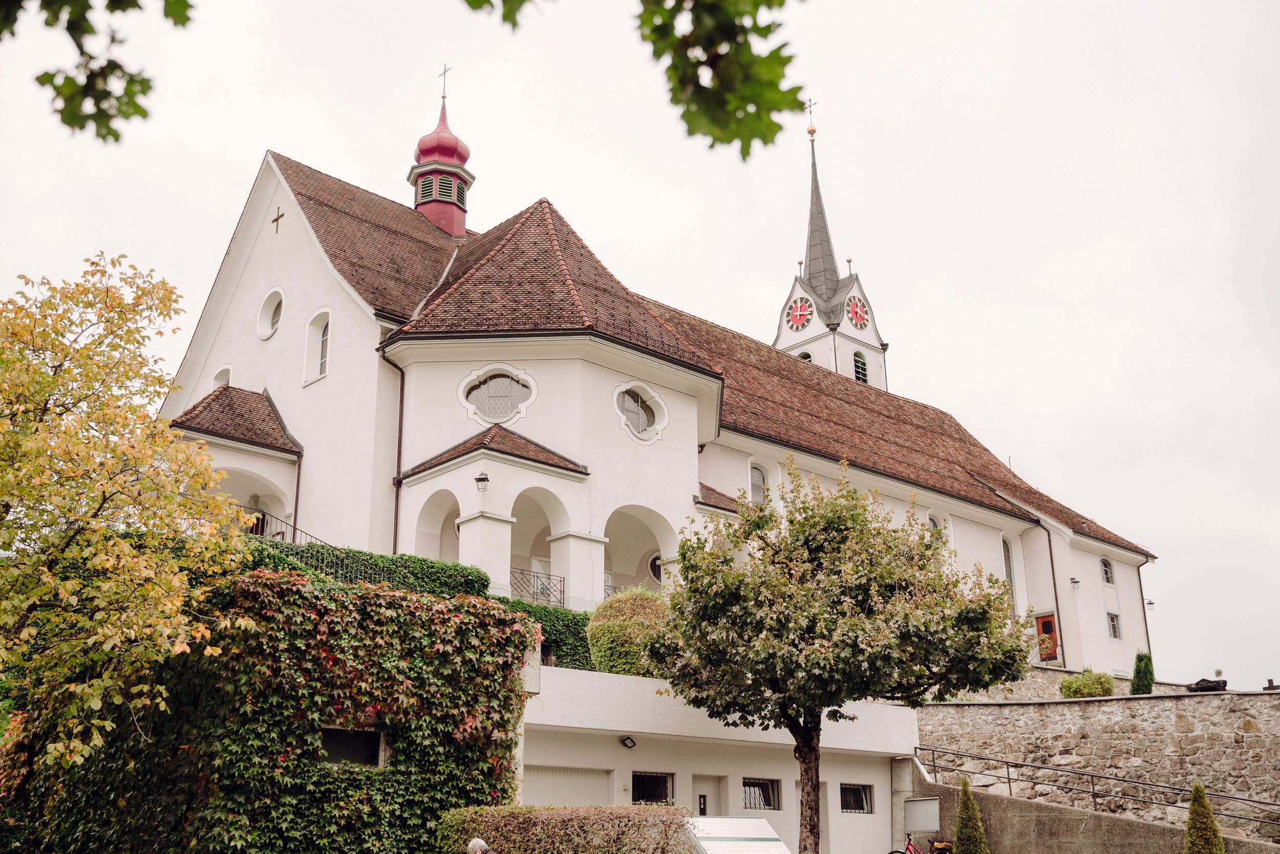 Wide shot of a historic white church and village buildings nestled in the green hills of Brunnen.