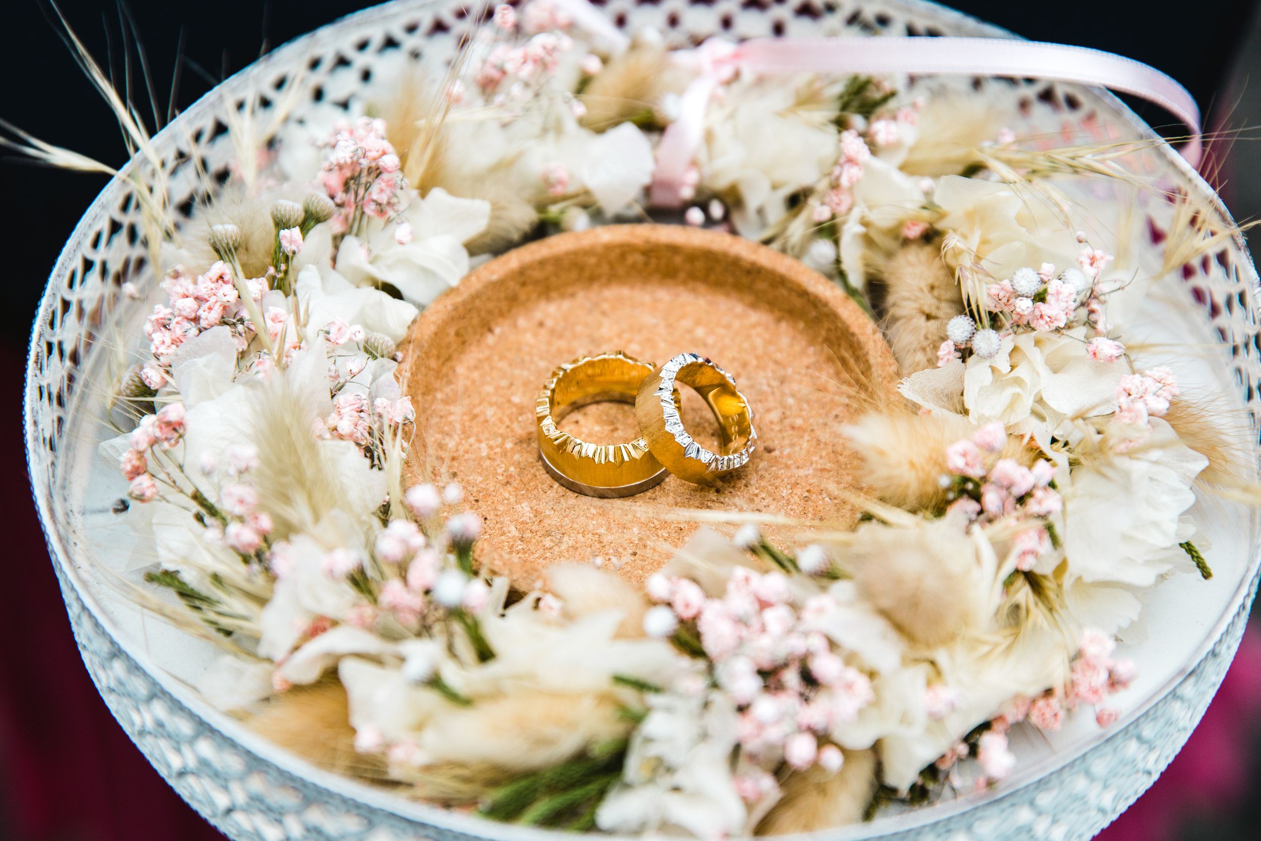 Close-up detail of two gold wedding rings presented in a white bowl with fresh flower petals.