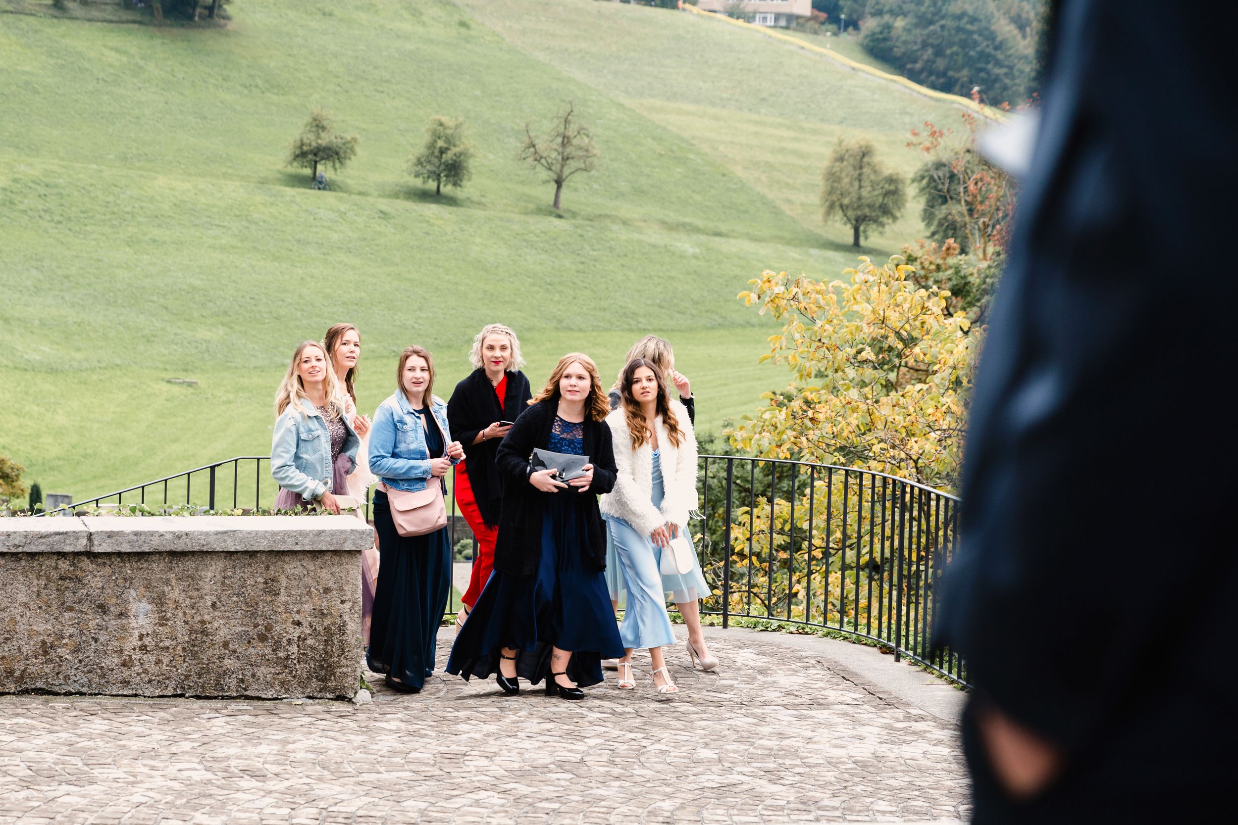 Candid shot of a small group of wedding guests standing on a stone terrace overlooking green hills.