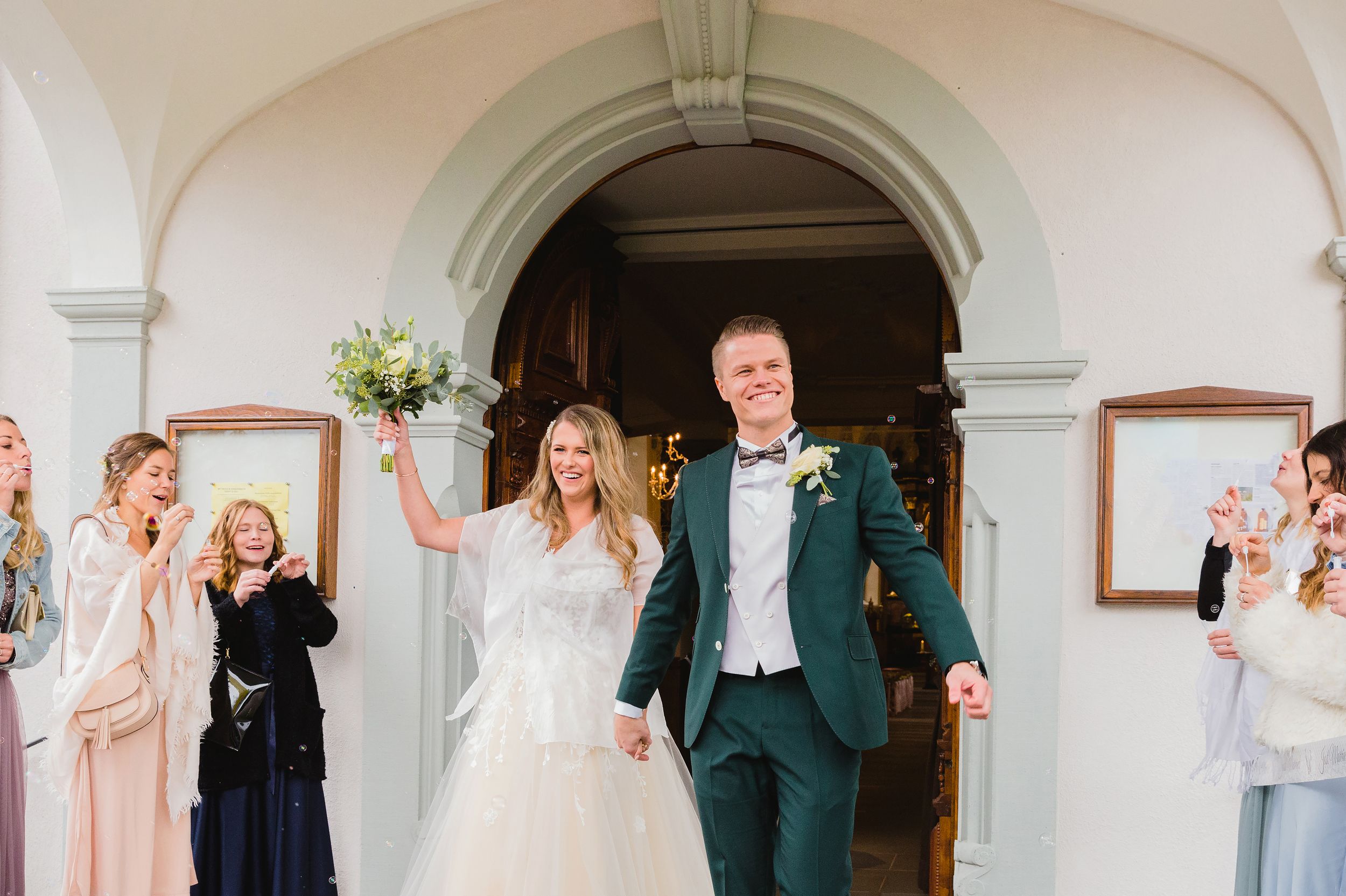 Bride and groom smiling and walking through a cheering crowd under a grand archway at their wedding in Brunnen.