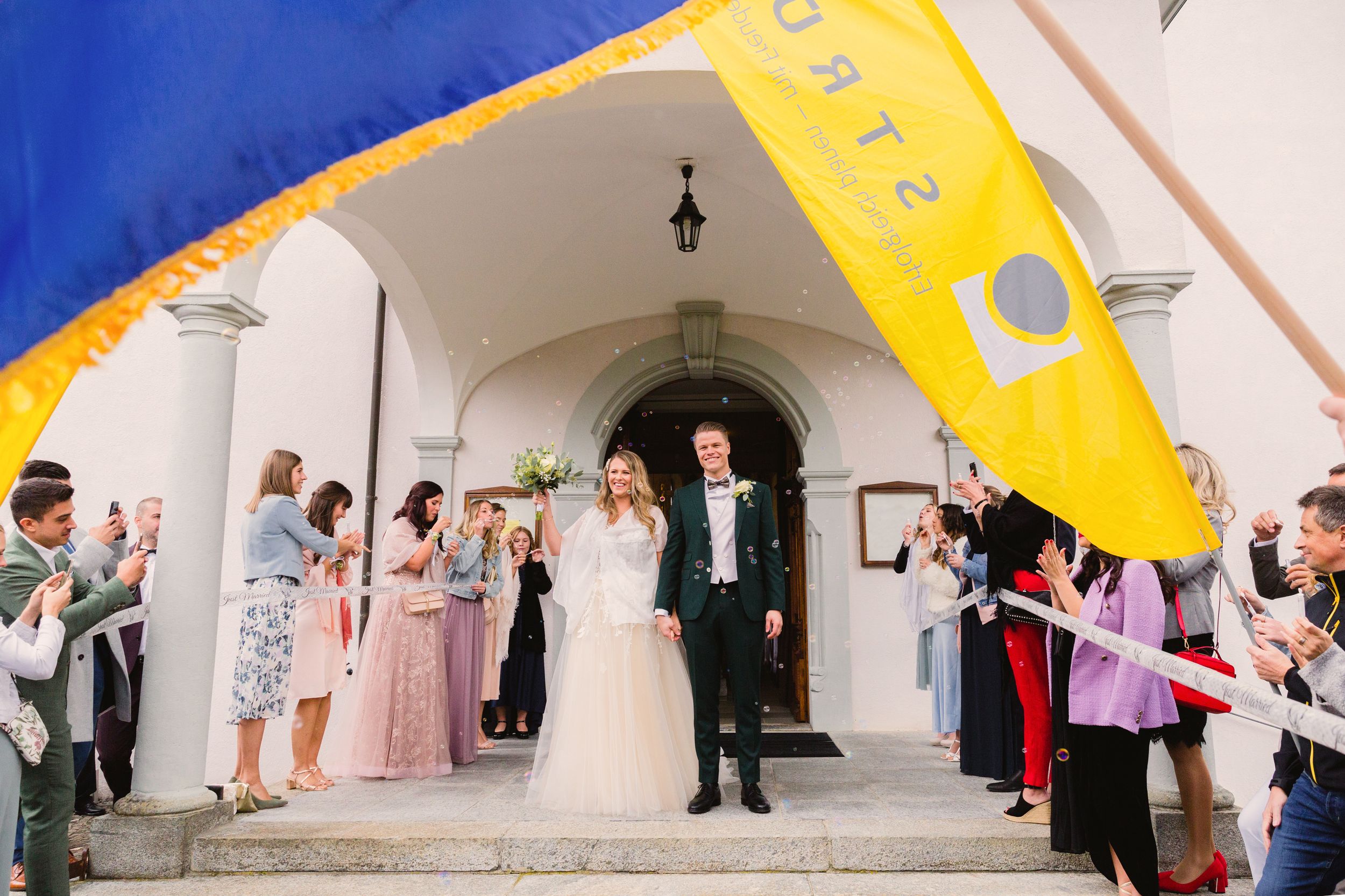 Wedding guests forming a celebratory archway with yellow banners for the bride and groom's grand exit.