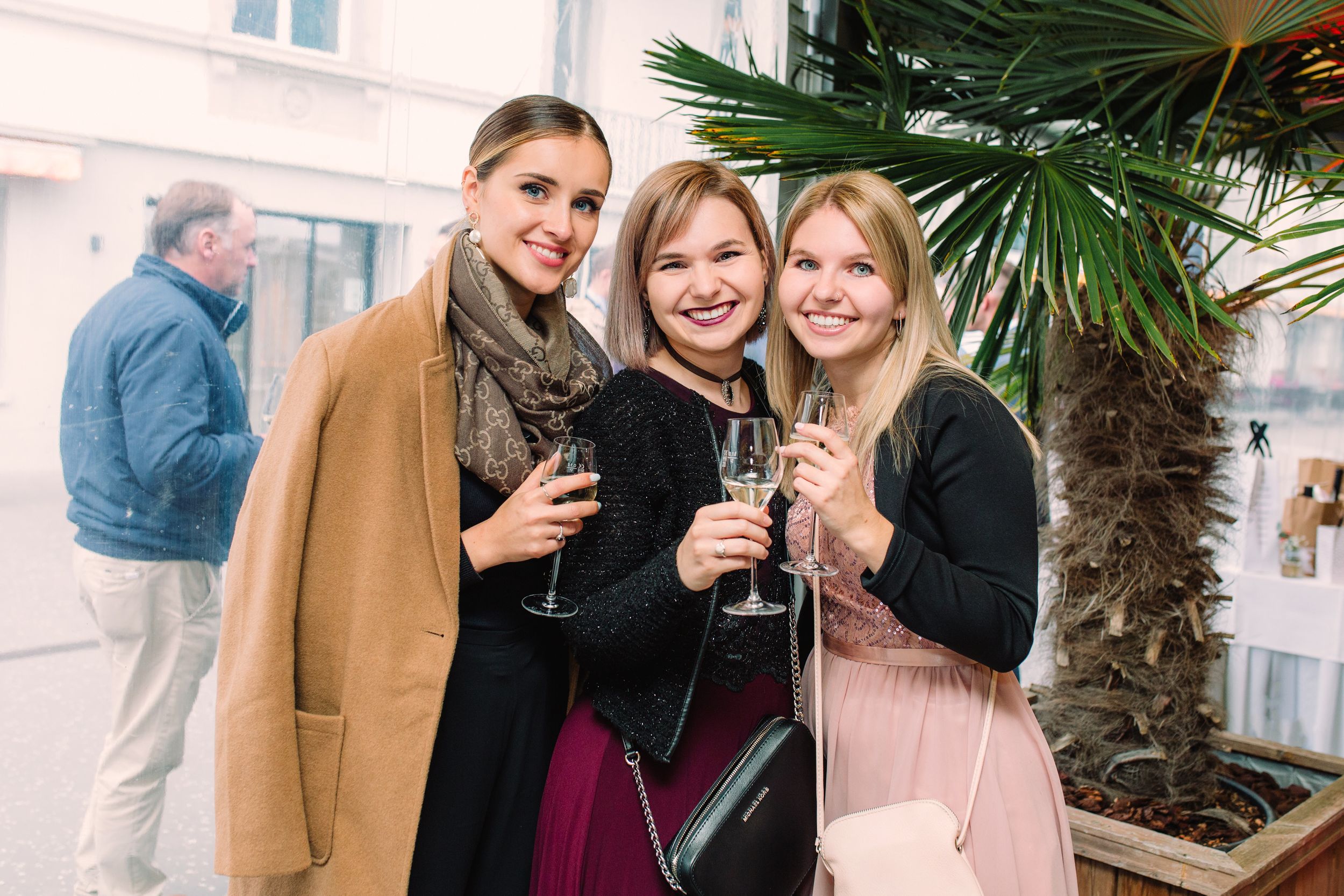 Three women sharing a drink and smiling during an outdoor wedding celebration in a scenic location.