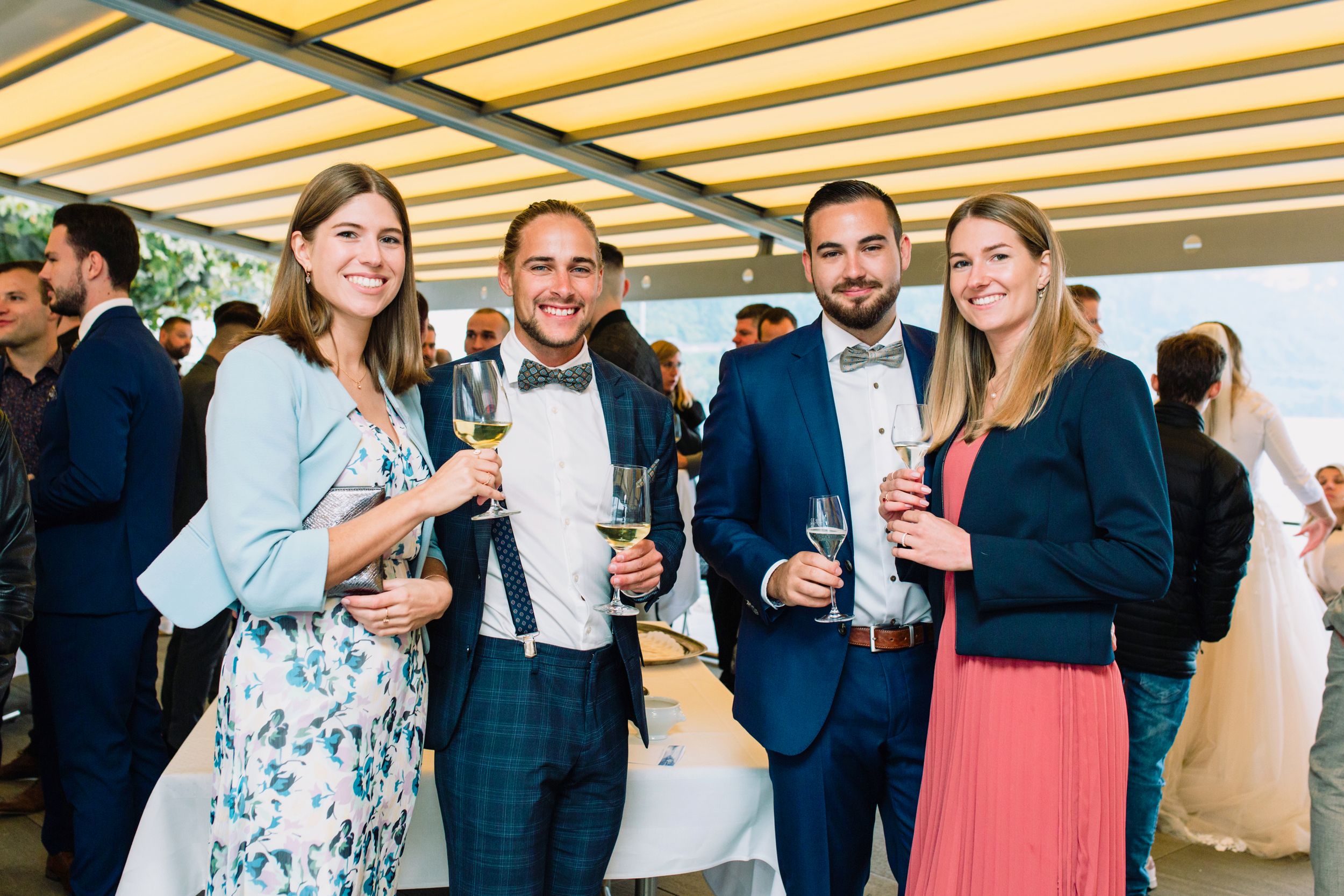 Candid shot of wedding guests smiling and mingling under a sun-drenched outdoor canopy.