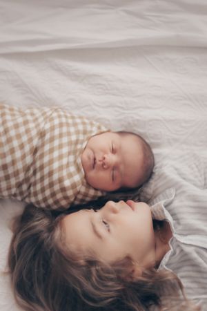 Two peaceful figures resting together on soft white bedding with gingham patterns.