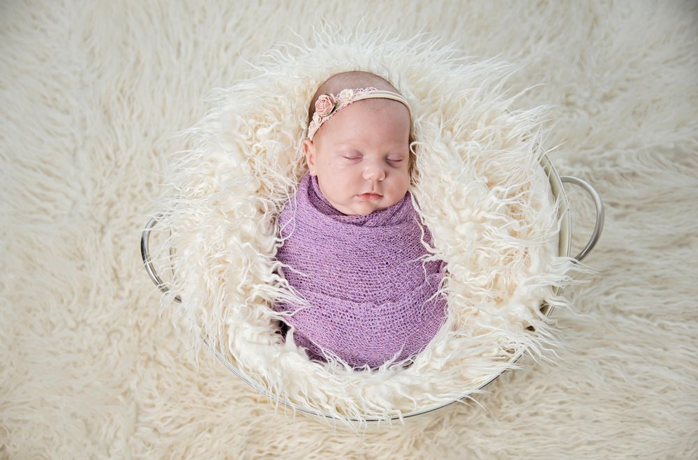 Creative newborn posing in a vintage bowl with soft wool textures.
