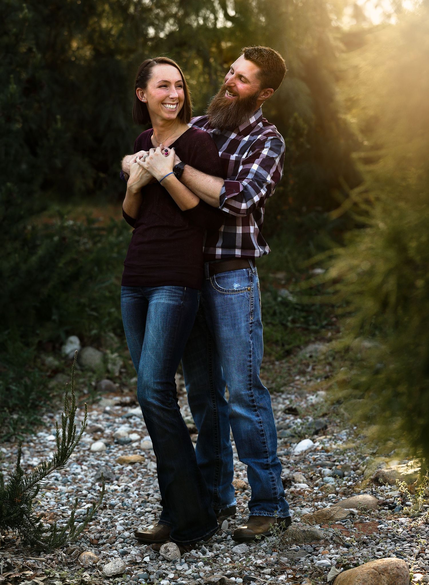 Couple embracing on rocky path during golden hour in forest.