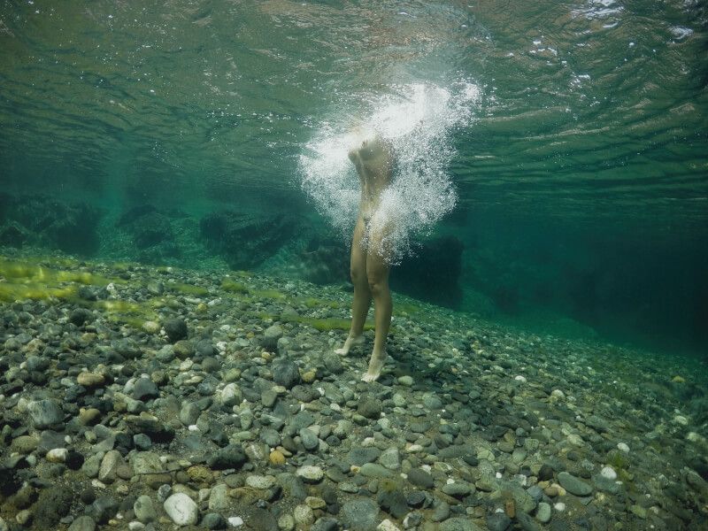 Underwater photograph of swimmer in clear turquoise water over rocky riverbed.