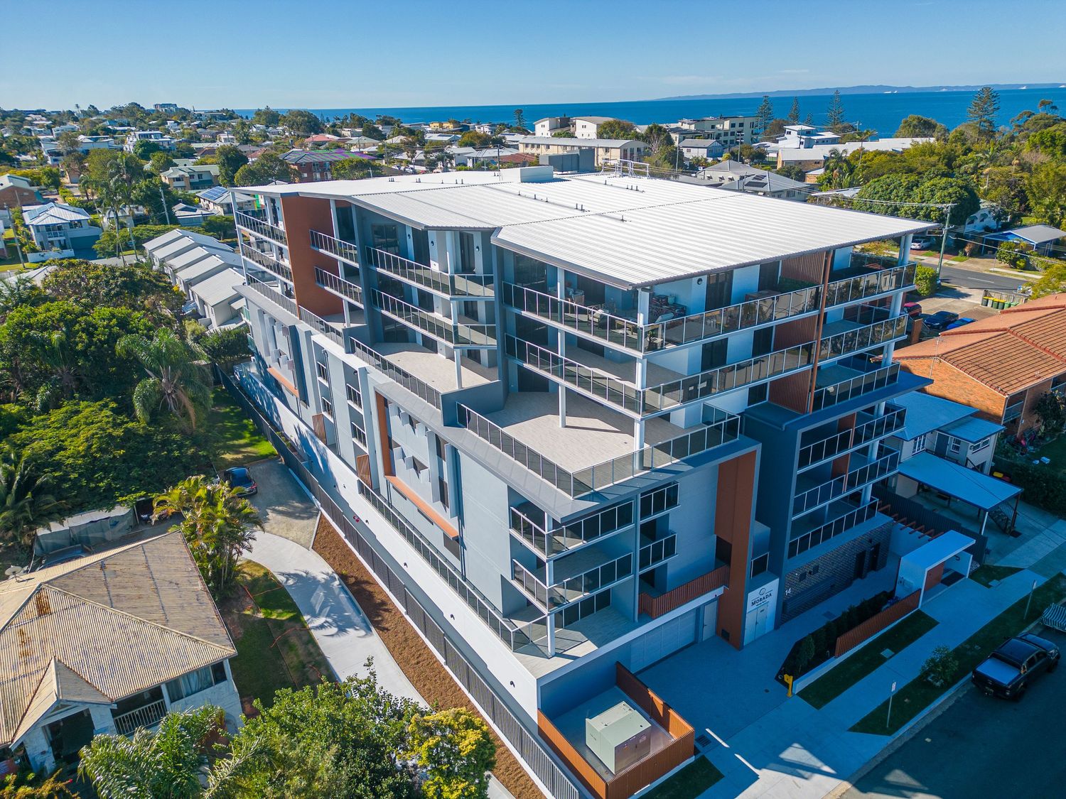 Modern waterfront apartment building with white and brown exterior and multiple balconies.