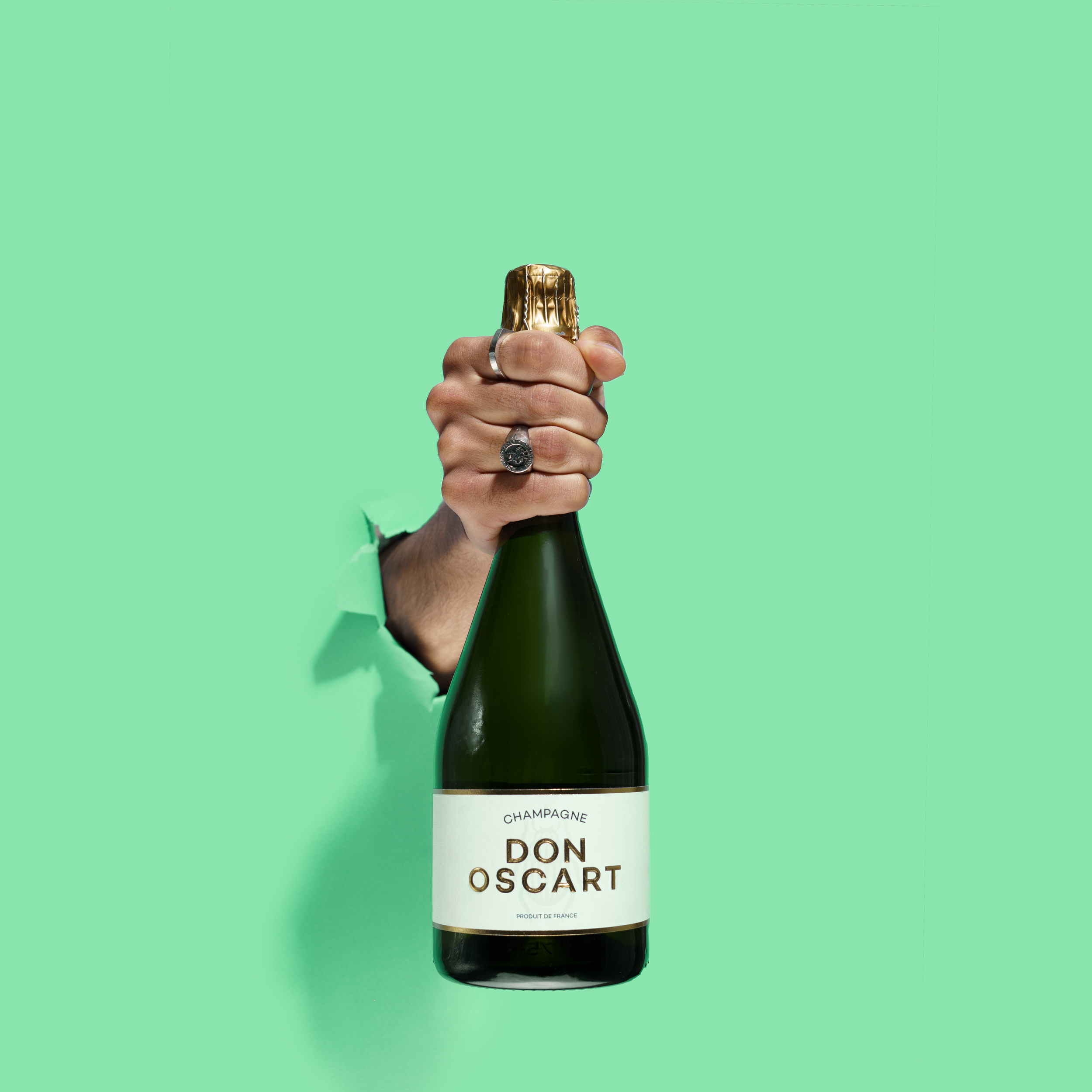 Green-tinted promotional photo of hands gripping Don Oscart bottle against mint background.