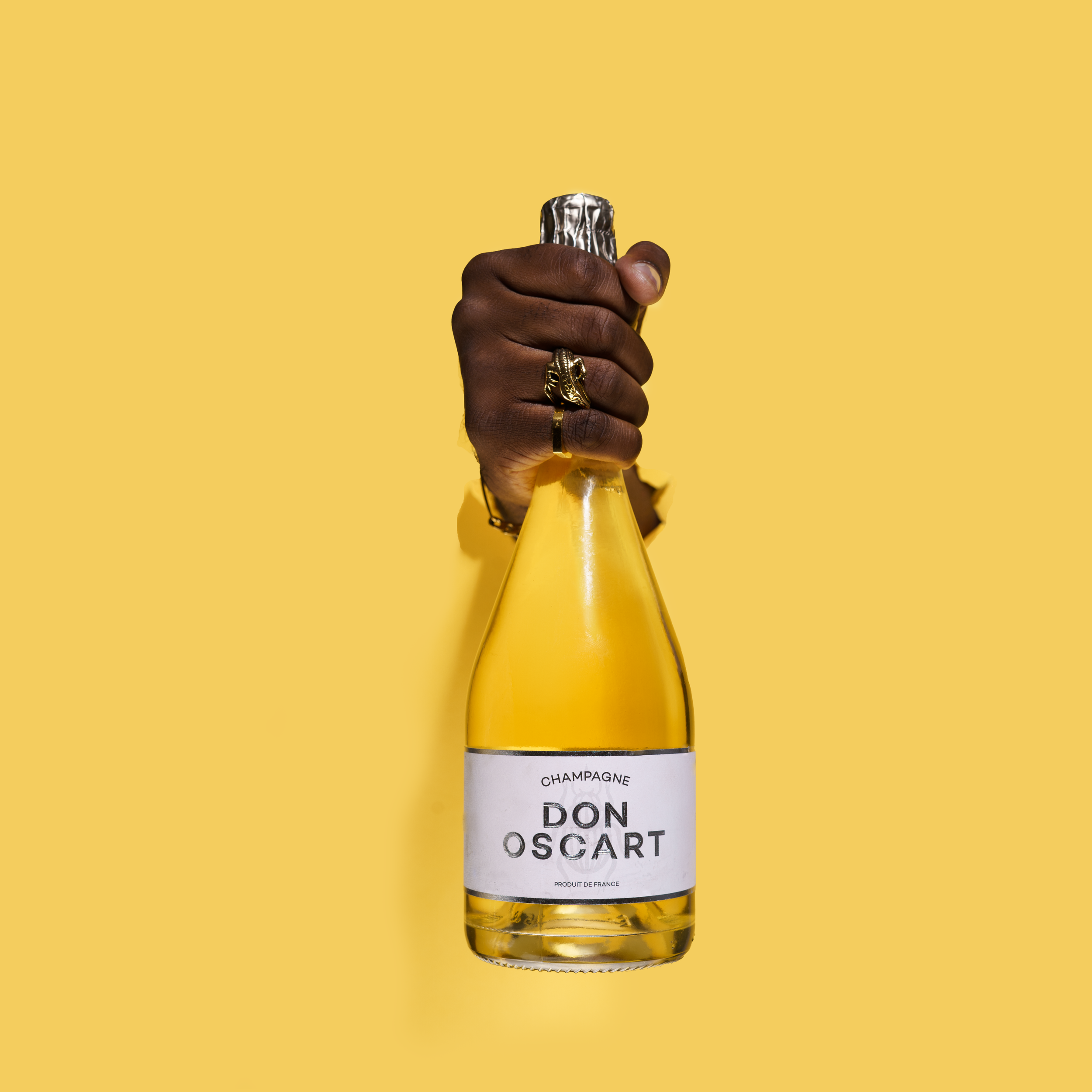 Bottle of Don Oscart beverage held by hand against yellow background.