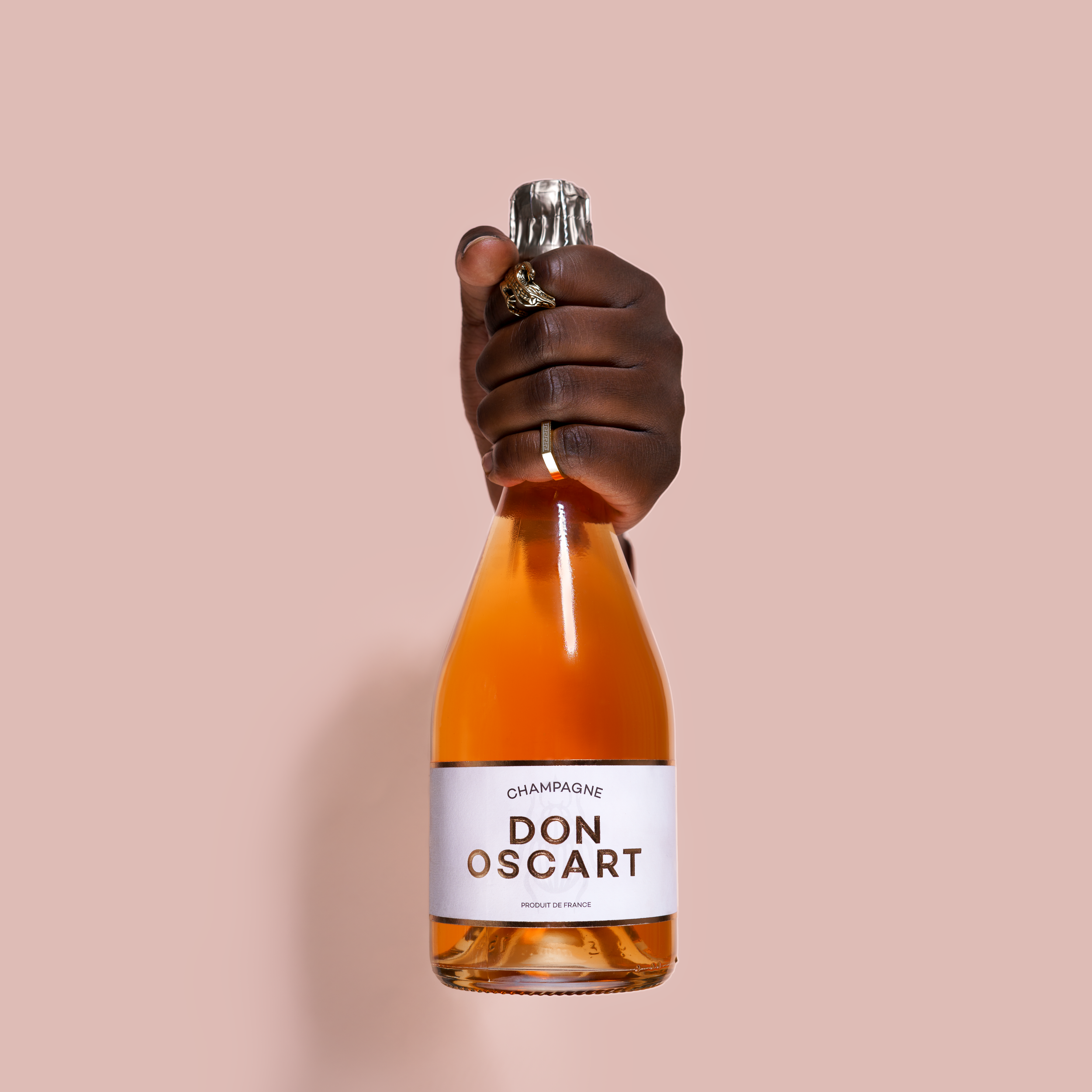 Orange bottle of Don Oscart held by hands against pink background.