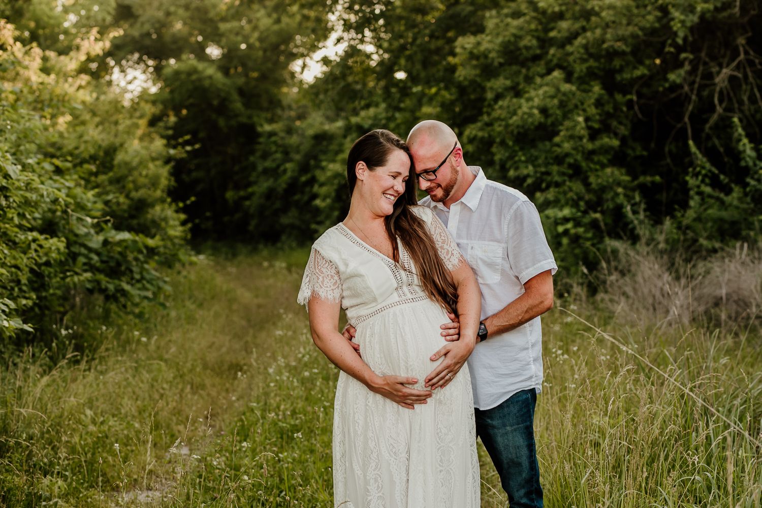 Maternity photoshoot in a wildflower meadow with couple in casual attire.