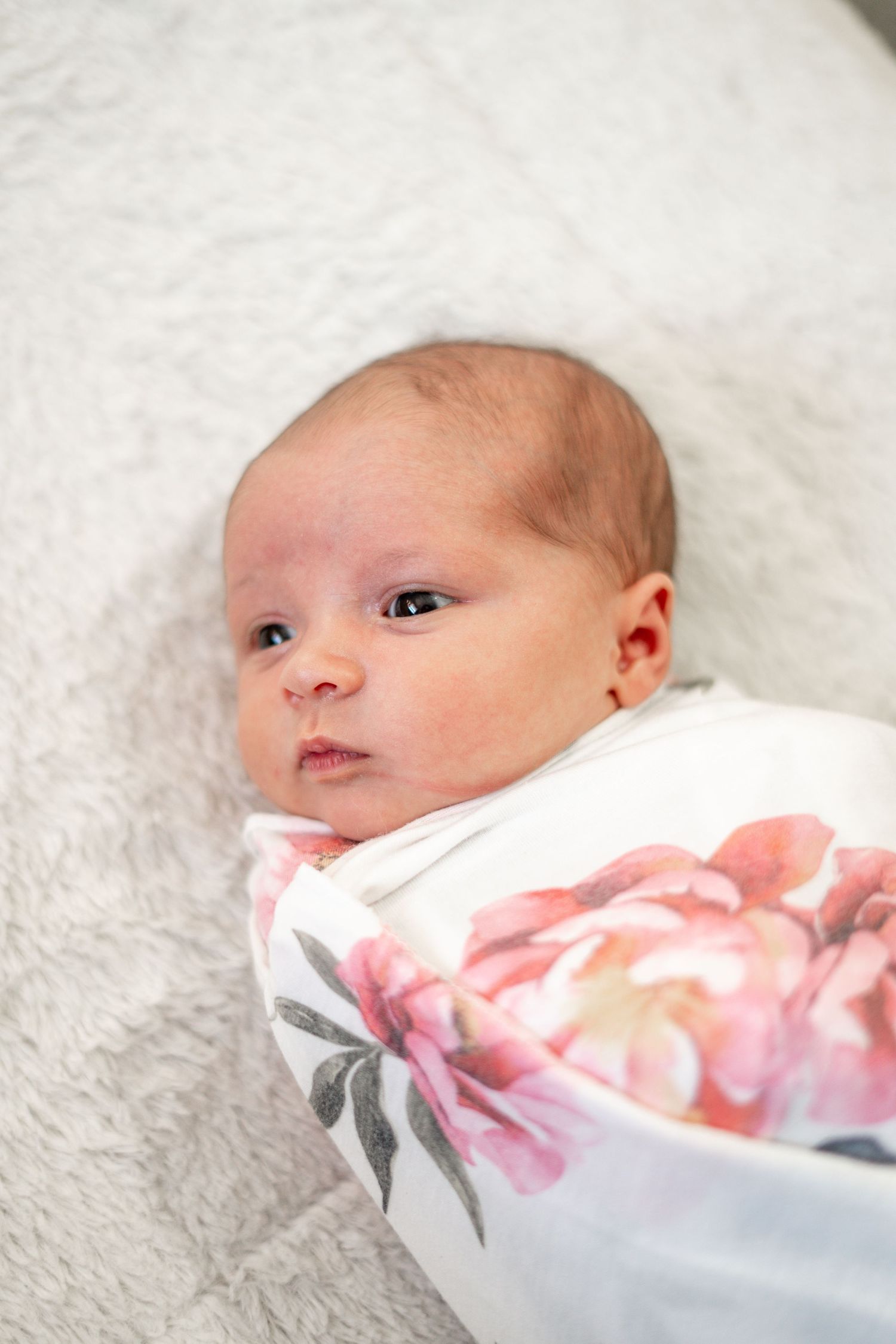 Close-up of a newborn baby wrapped in a floral blanket on white bedding.