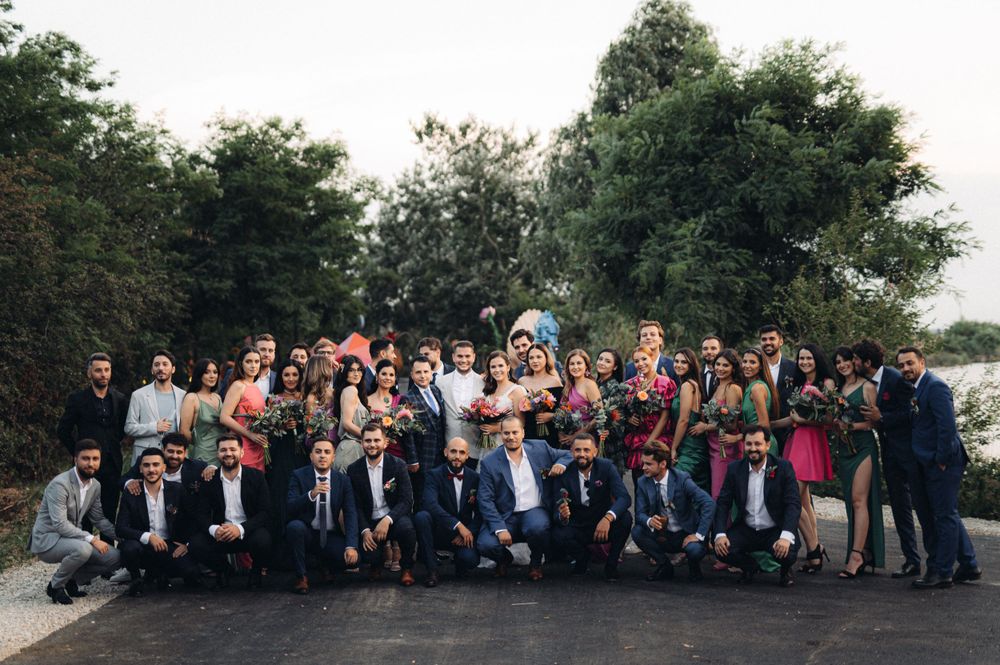 Large wedding group photo with guests in formal attire on outdoor path.