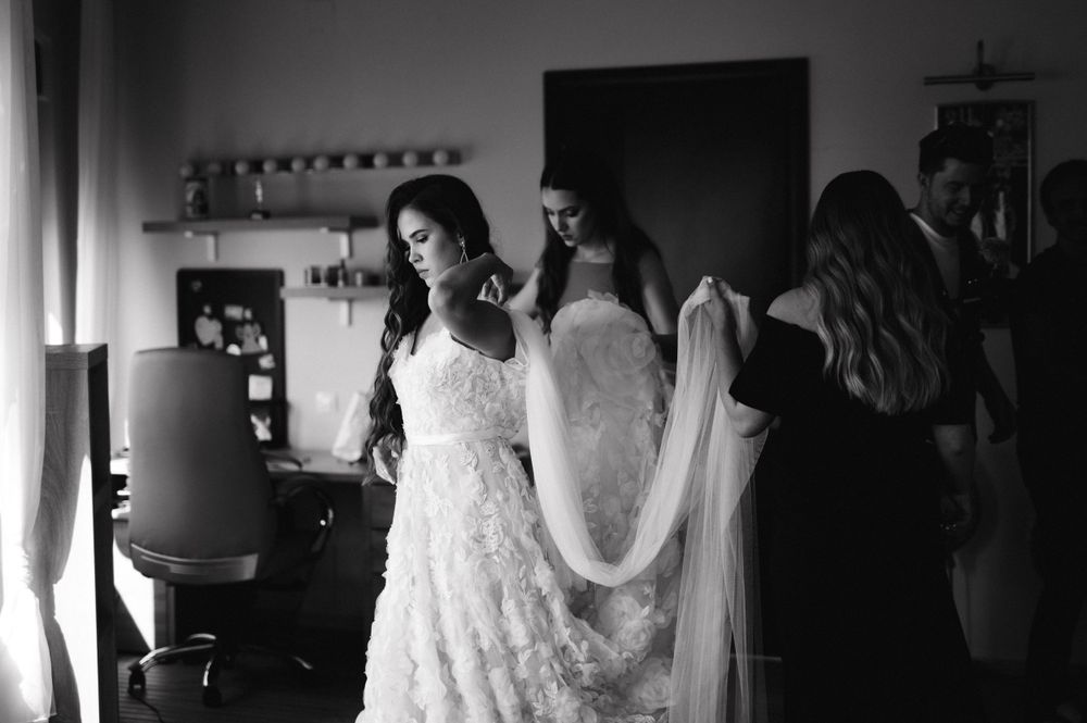 A black and white photo capturing final preparations of a bride in her lace wedding gown.