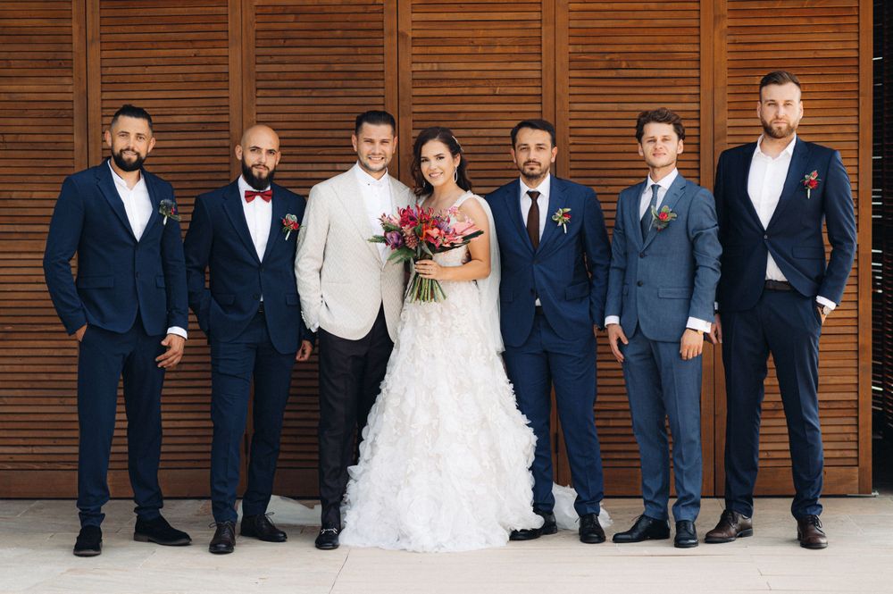 Wedding party in formal attire poses against wooden wall backdrop.