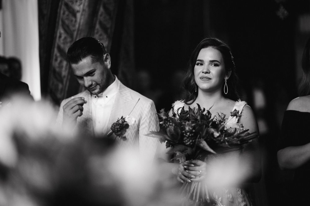 Black and white photo of a couple during their wedding ceremony with bouquet in focus.