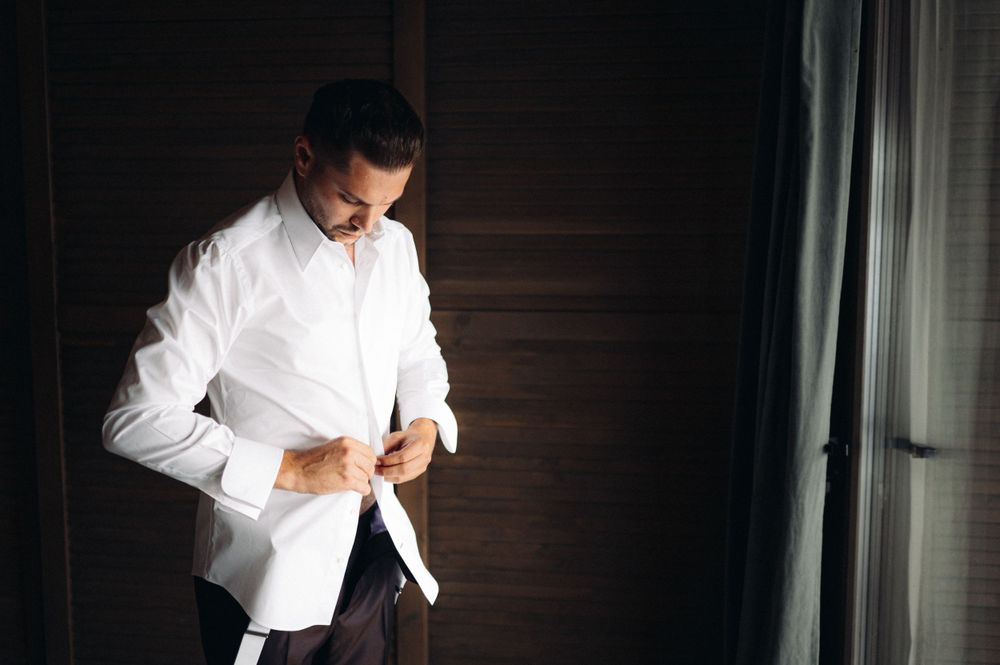 A person in a crisp white dress shirt adjusting their cuffs in dim lighting.