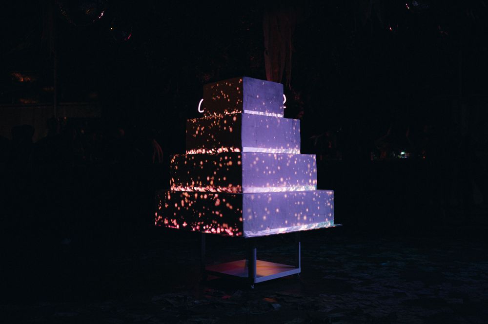 Illuminated tiered wedding cake with purple lighting and sparkle effects in a dark reception venue.