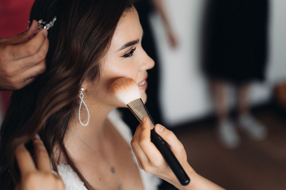 Makeup artist applies cosmetics on a bride wearing drop earrings during wedding preparations.