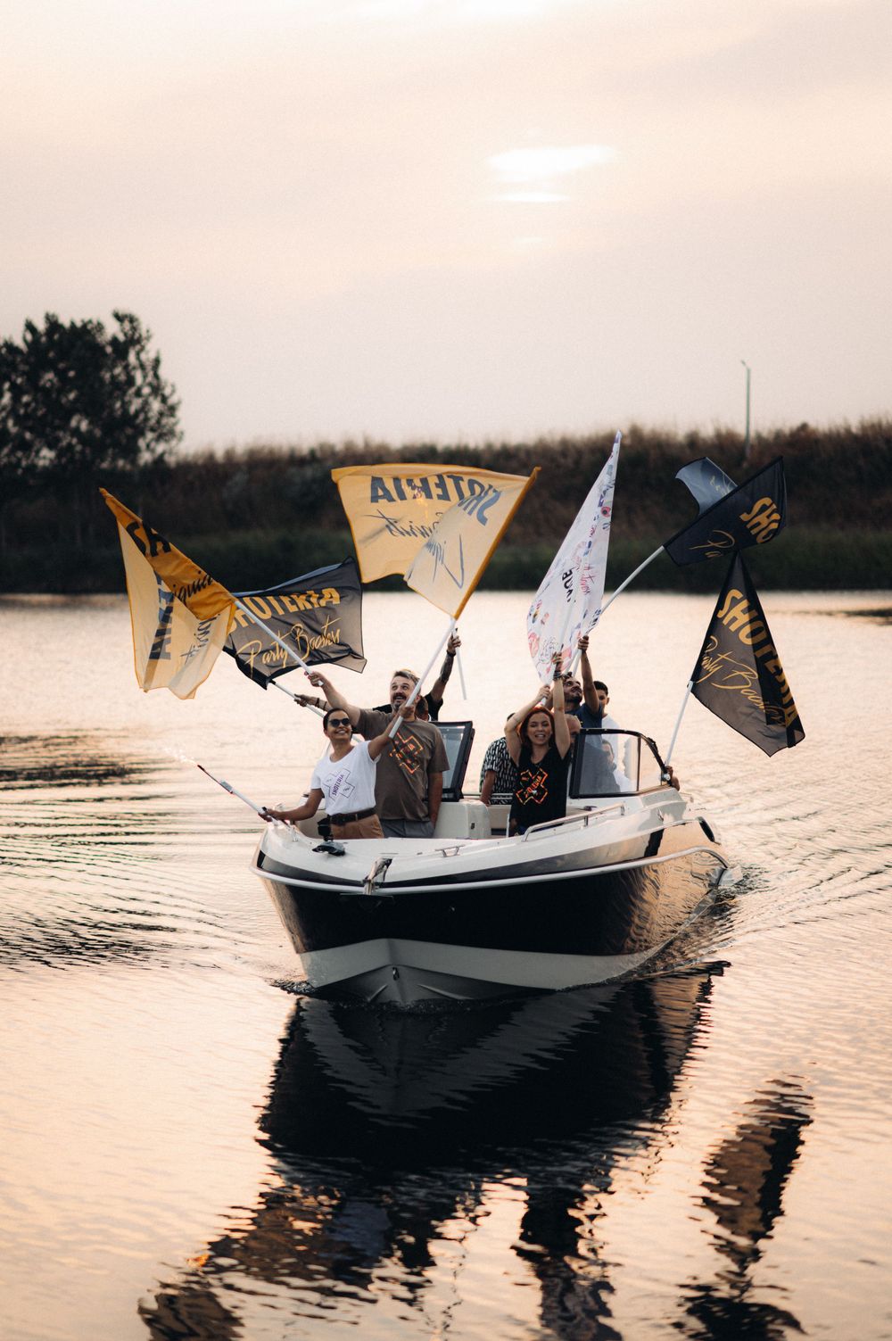Boat on lake at sunset carrying passengers waving flags and banners.