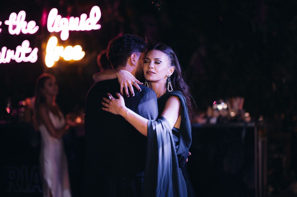 Two dancers embrace in an intimate slow dance under glowing lights at evening event.