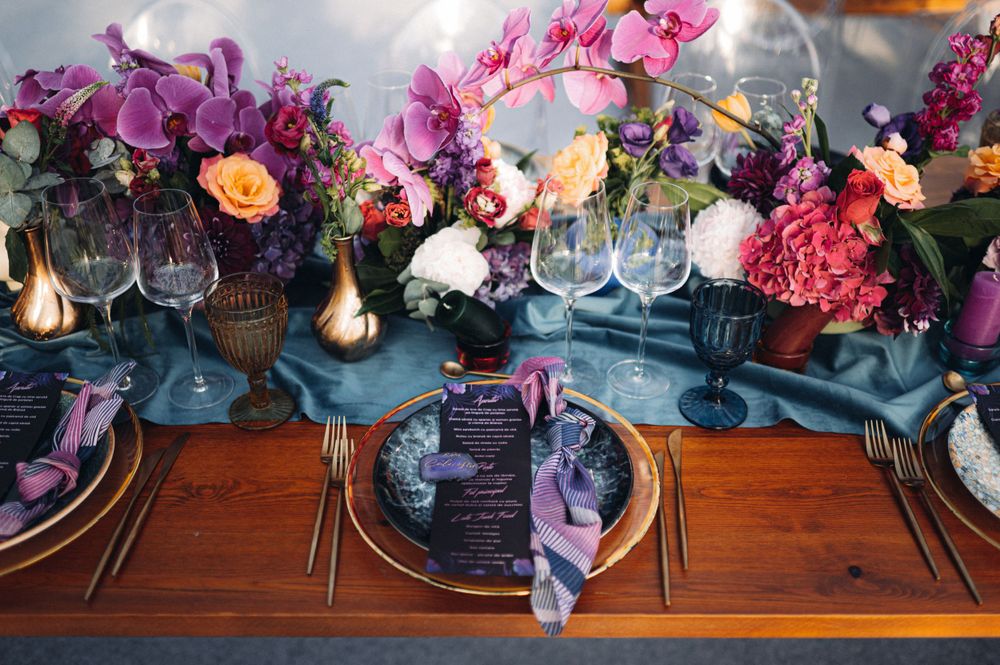 Elegant table setting with vibrant floral arrangements and purple accents for wedding reception.