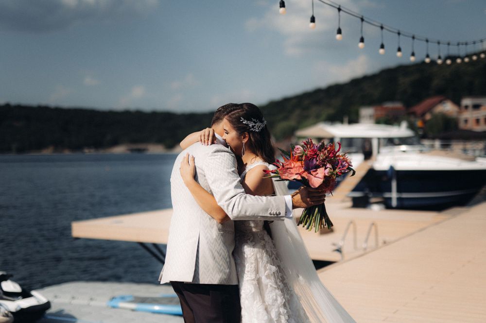 Romantic waterfront wedding moment with couple embracing against marina backdrop.